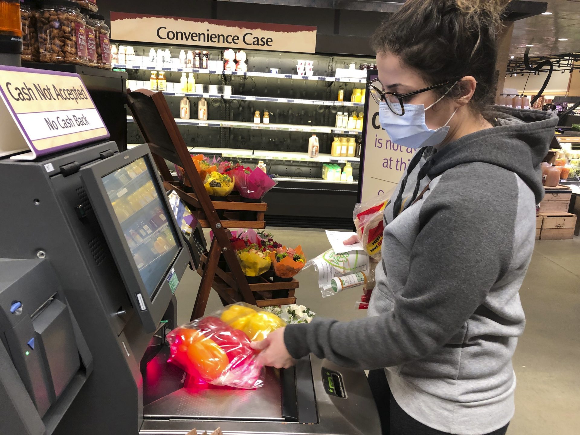 Wearing a surgical mask, Melissa Hall checks out of a Wegmans supermarket, Friday, March 13, 2020 in King of Prussia, Pa., Gov. Tom Wolf ordered schools, community centers, gyms and other venues in Montgomery County, a Philadelphia suburb, to shut down for two weeks amid a concentration of novel coronavirus cases there.