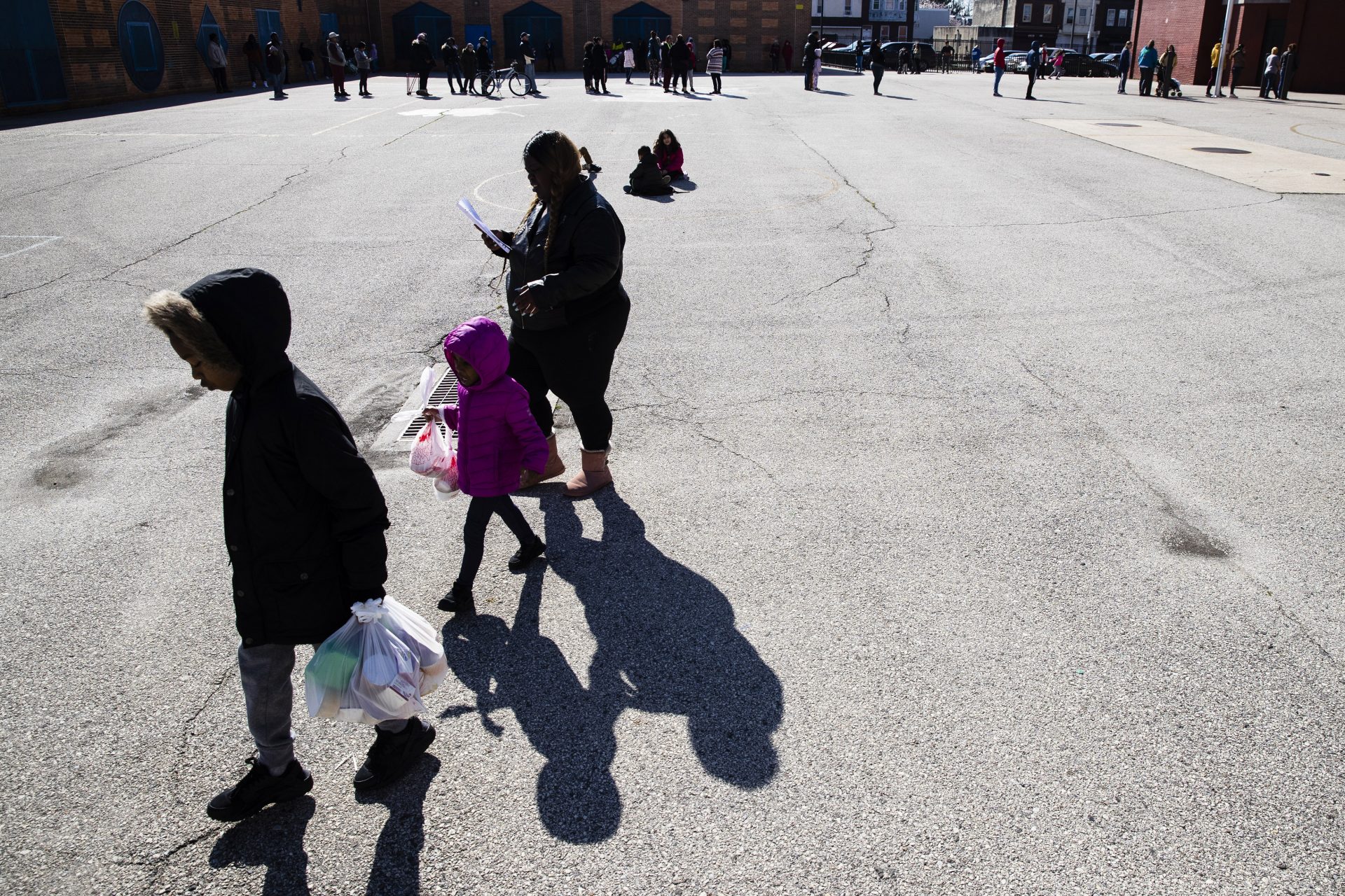 A woman and children walk away from the John H. Webster Elementary School carrying donated food and educational materials, in Philadelphia, Thursday, March 26, 2020.