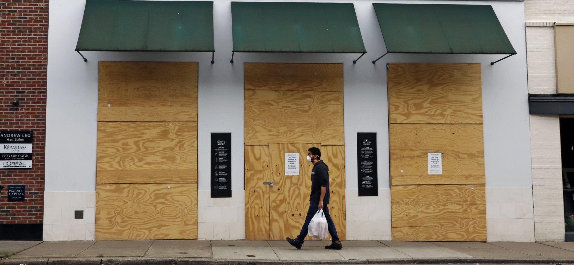 FILE PHOTO: A man walks in the Shadyside shopping district of Pittsburgh past a Williams-Sonoma store that is boarded up temporarily due to social distancing mandated due to COVID-19 coronavirus on Wednesday, April 29, 2020.