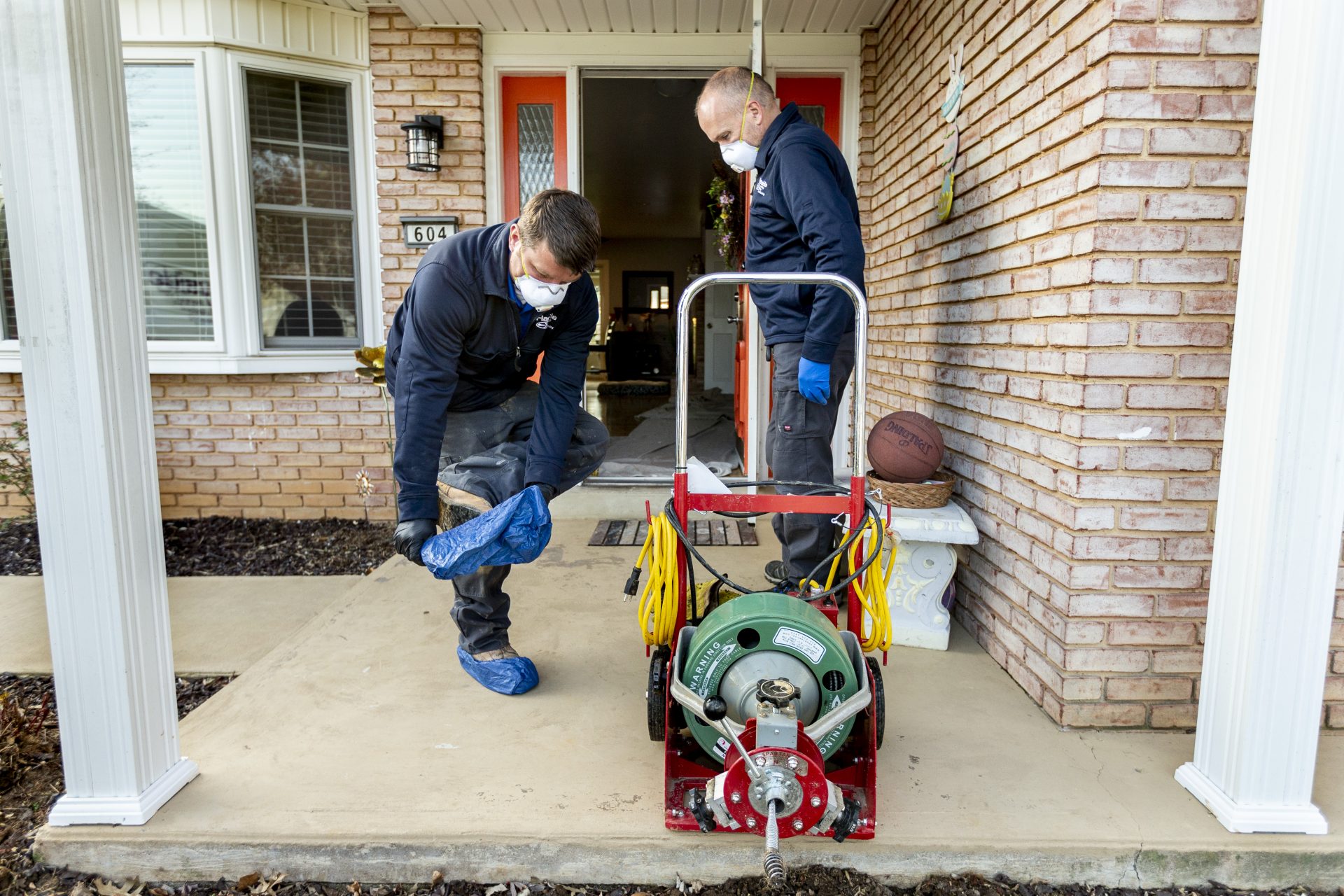 Shawn Stokes and Roger Renoll of Handyside Plumbing, HVAC & Electrical put on protective gear before entering a home in Mechanicsburg on April 7, 2020.
