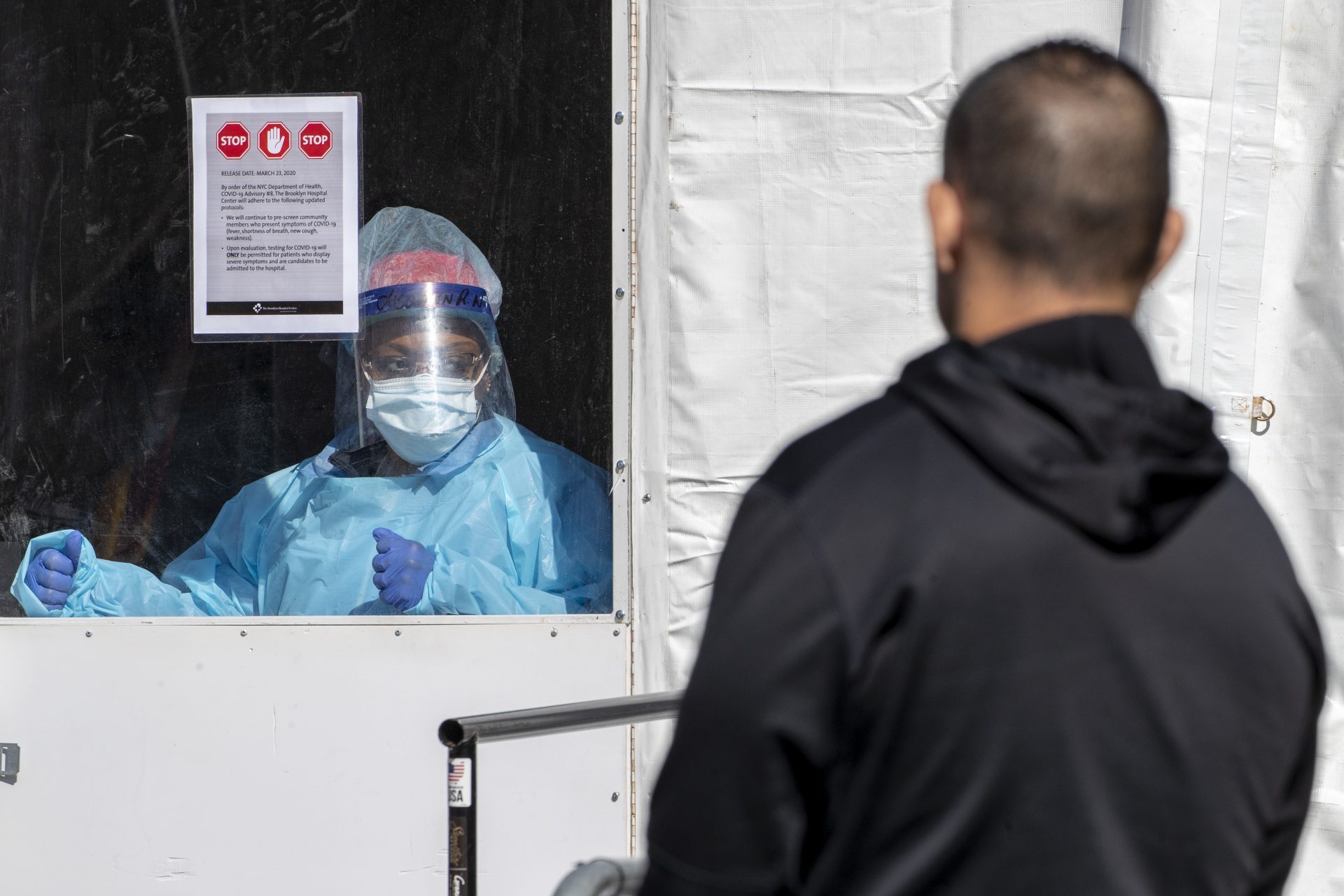 A member of the Brooklyn Hospital Center COVID-19 testing team calls in the next patient in line, Thursday, March 26, 2020, in the Brooklyn borough of New York. The new coronavirus causes mild or moderate symptoms for most people, but for some, especially older adults and people with existing health problems, it can cause more severe illness or death.