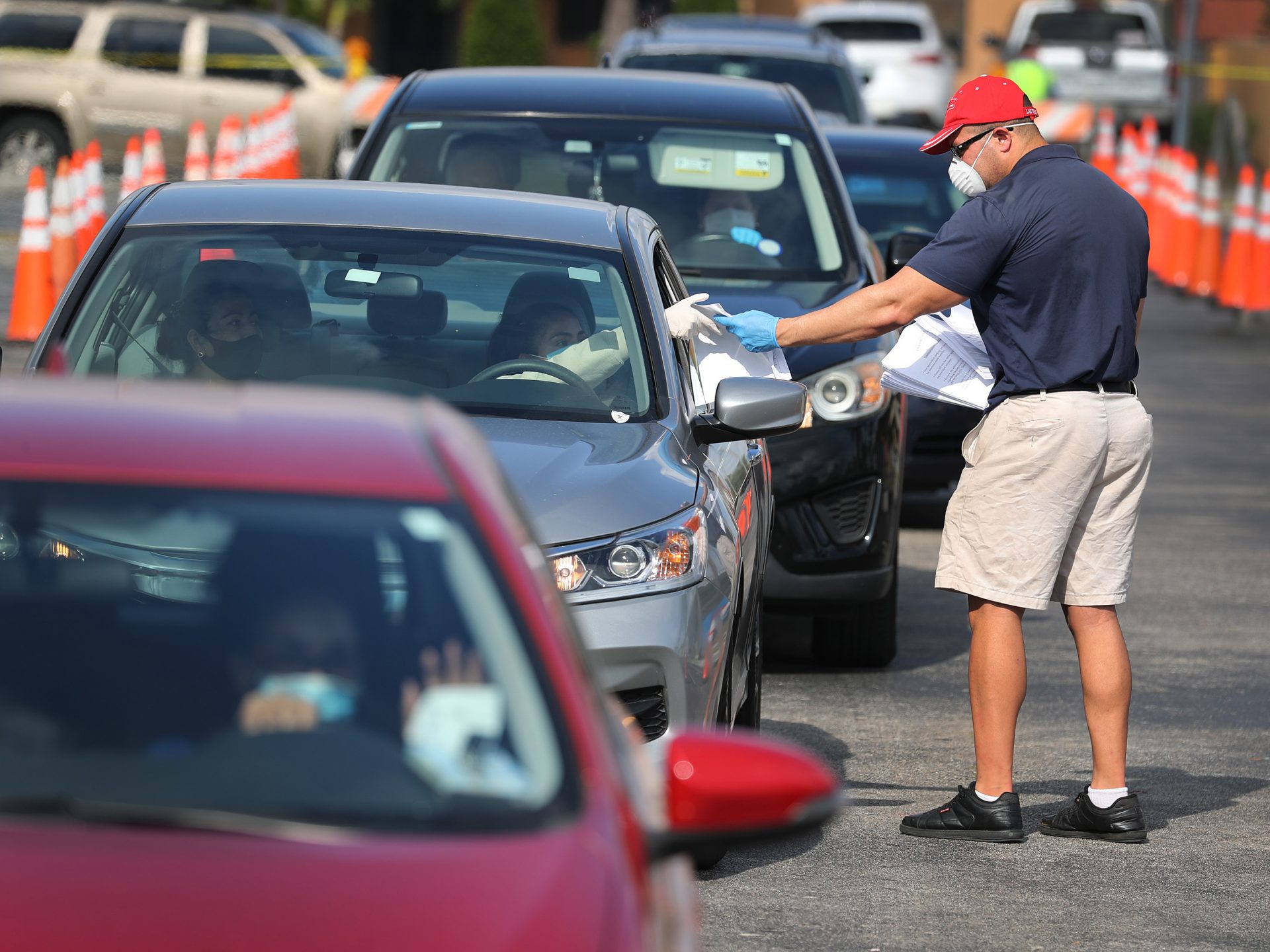 Miguel Diaz hands out unemployment applications to people in their vehicles on April 8 in Hialeah, Fla. Black, Latino and Asian American workers have lost jobs at a faster clip than white employees during the coronavirus pandemic.