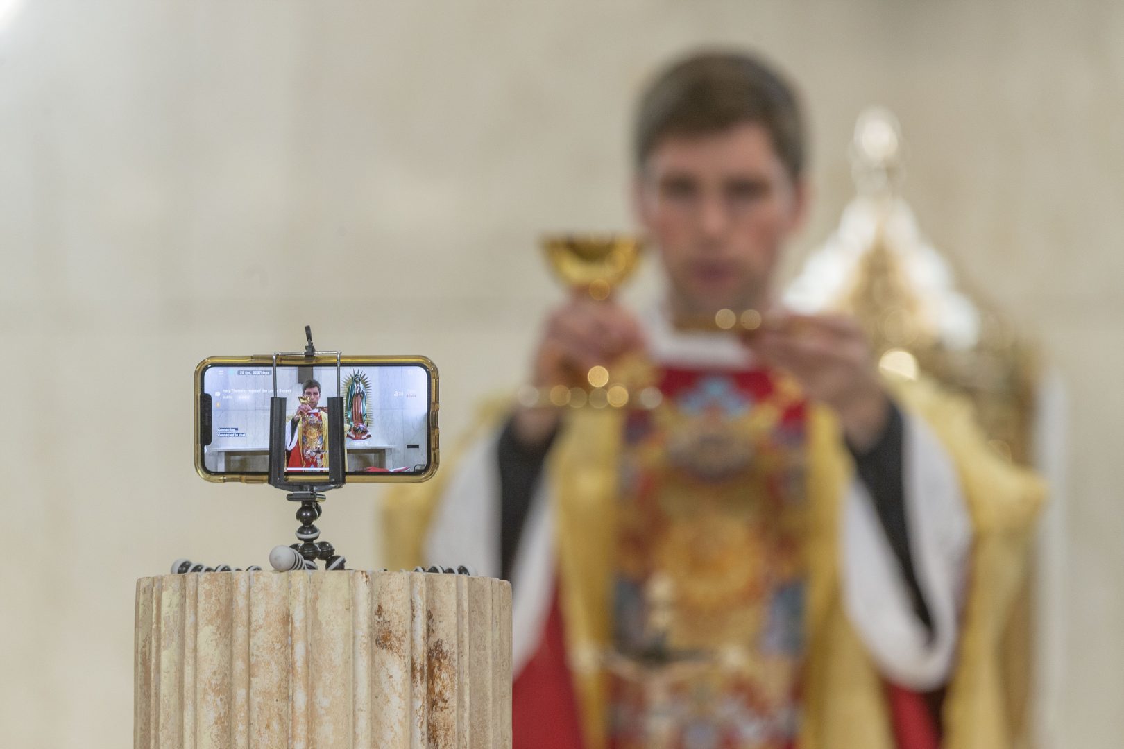 The Rev. Matthew Wheeler is seen on an iPhone screen live-streaming the celebration of the the Mass of the Lord's Supper at St. Anthony Parish in San Gabriel, Calif., Thursday, April 9, 2020. With no public Mass due to the coronavirus pandemic, the church live-streams its services.