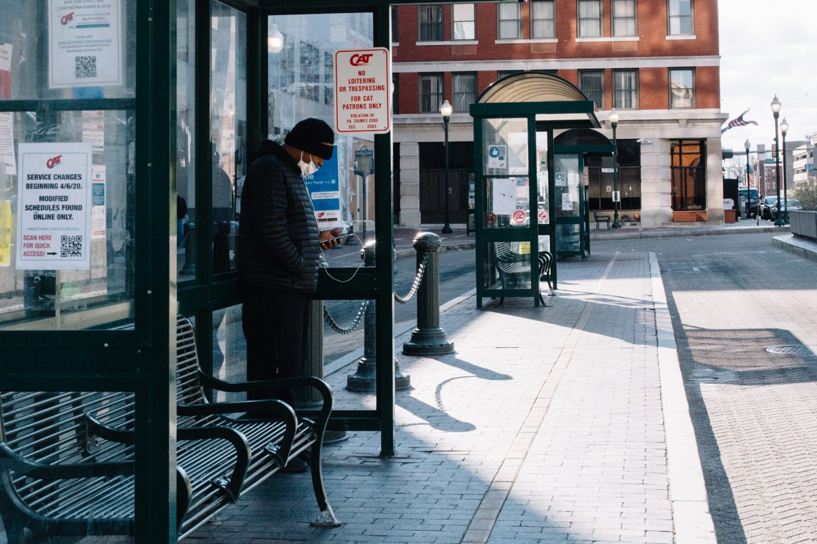 A man wearing a mask over his mouth checks his phone while waiting for a bus in Harrisburg on April 10, 2020.