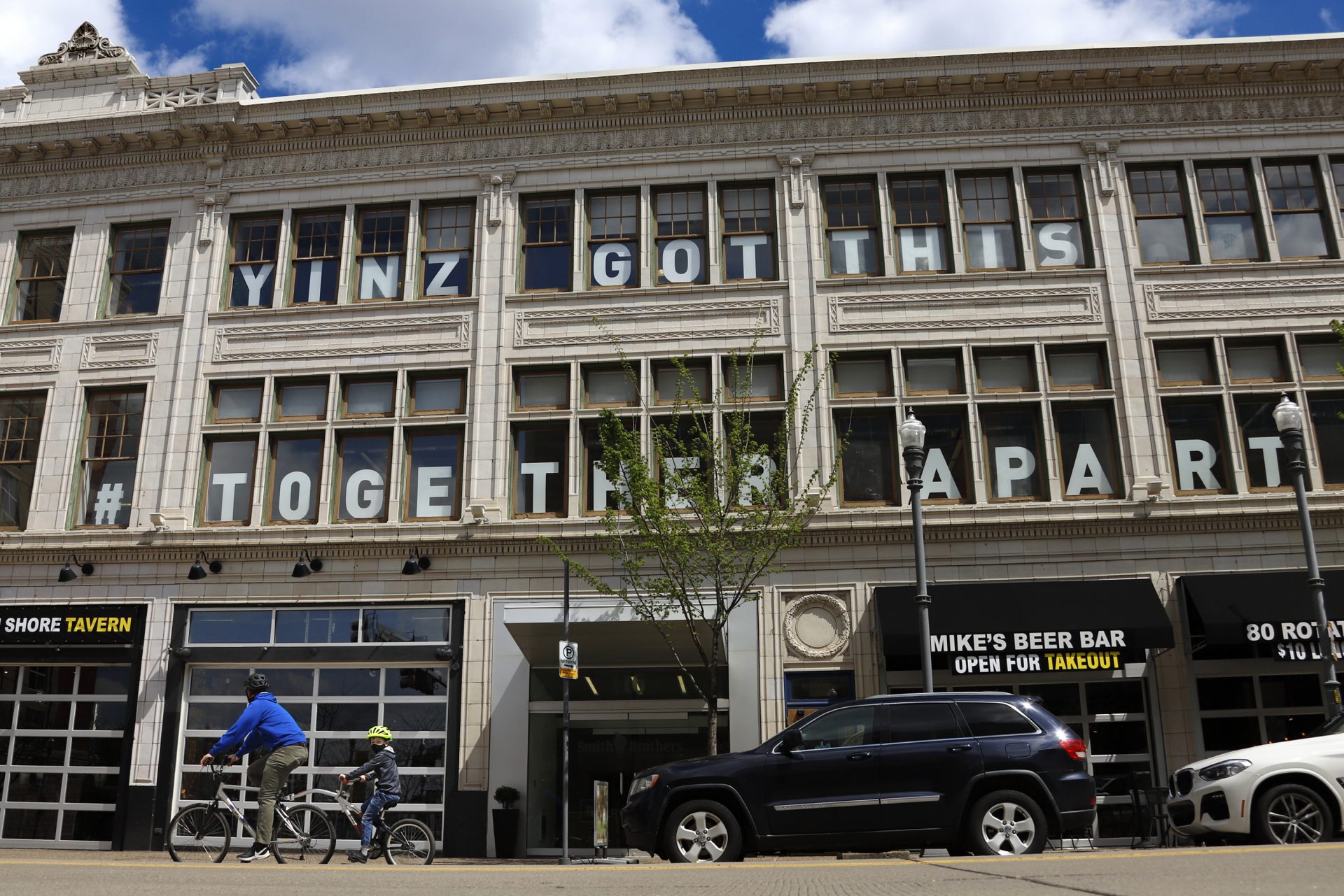 A father and son ride their bikes past a building on the Northside of Pittsburgh that sports a sign of encouragement for the efforts being made to mitigate the spread of COVID-19, Wednesday, April 15, 2020.