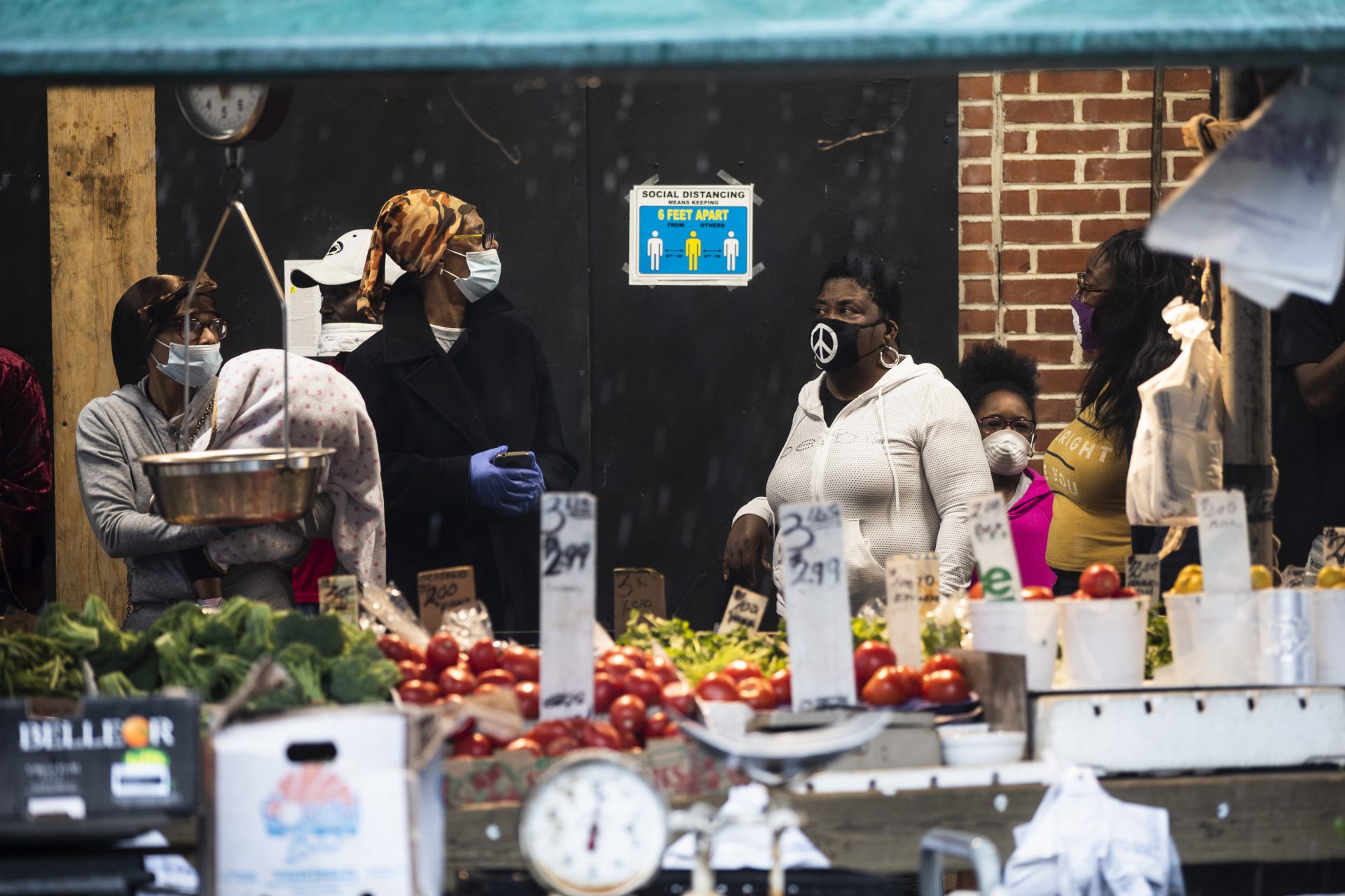 Shoppers wearing a face masks to protect against the spread of new coronavirus, wait in line to enter a store on South 9th Street in Italian Market neighborhood of Philadelphia as it rains, Thursday, April 9, 2020.
