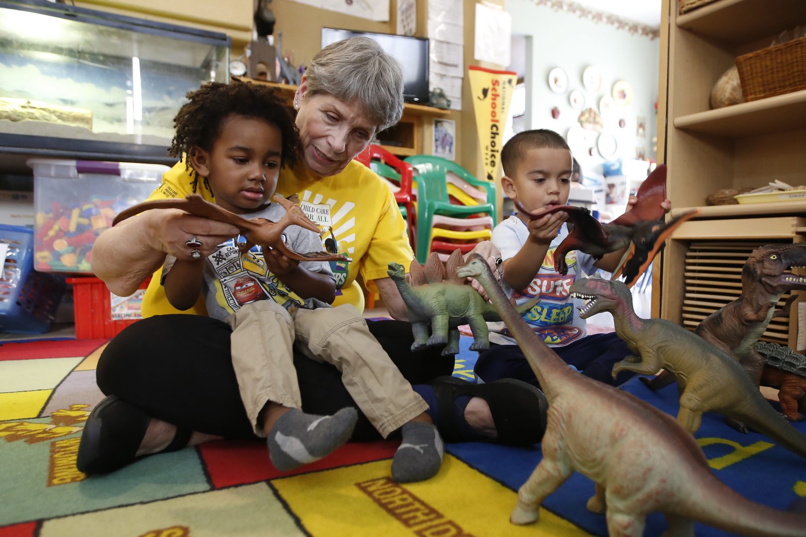Child care provider Pat Alexander helps children, Isaiah, left, and Hector, right, identify various types of dinosaurs at her child care center in Elk Grove, Calif., on Wednesday, Feb. 26, 2020.