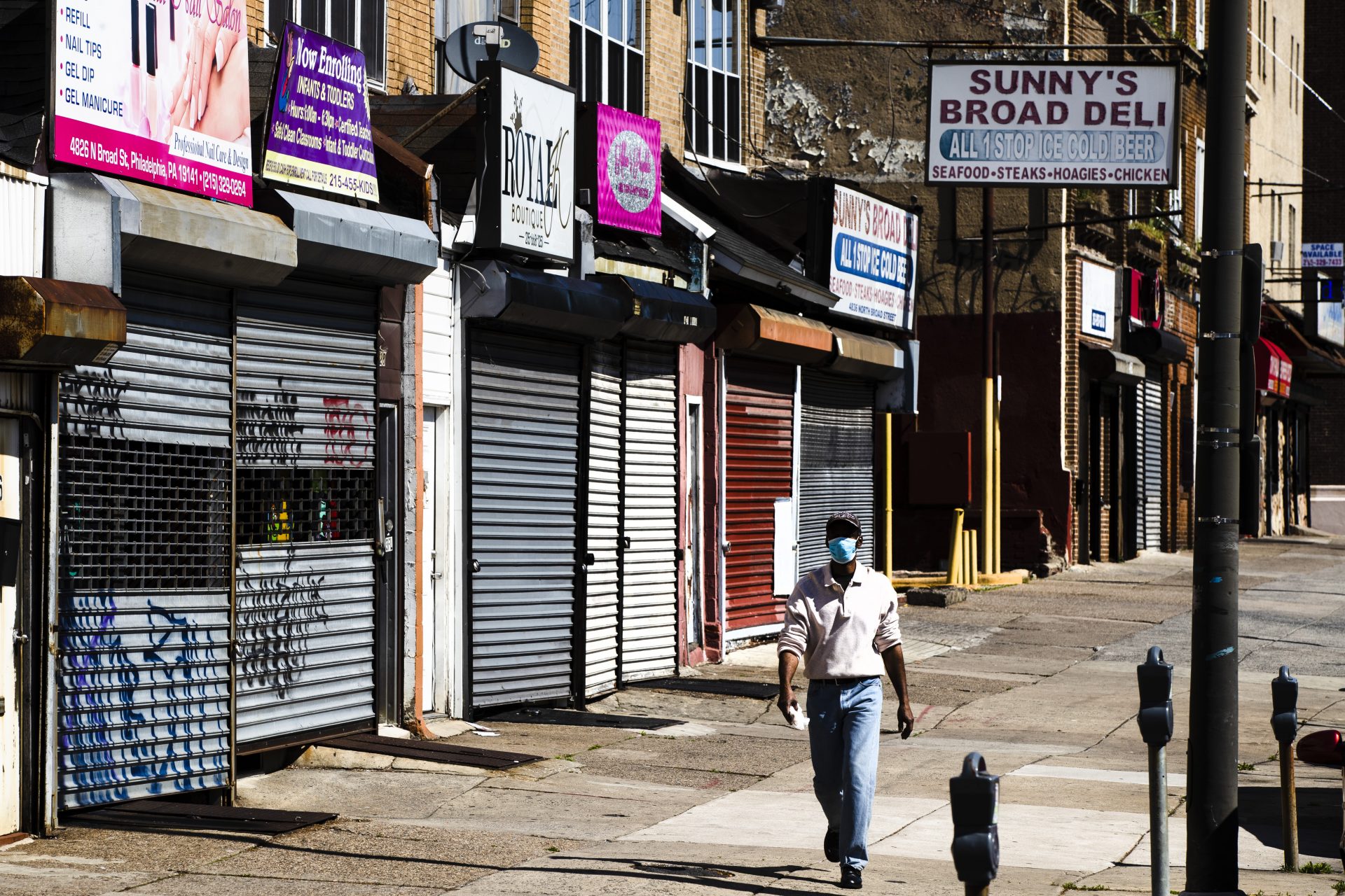 A person wearing a protective face mask as a precaution against the coronavirus walks past stuttered businesses in Philadelphia, Thursday, May 7, 2020.