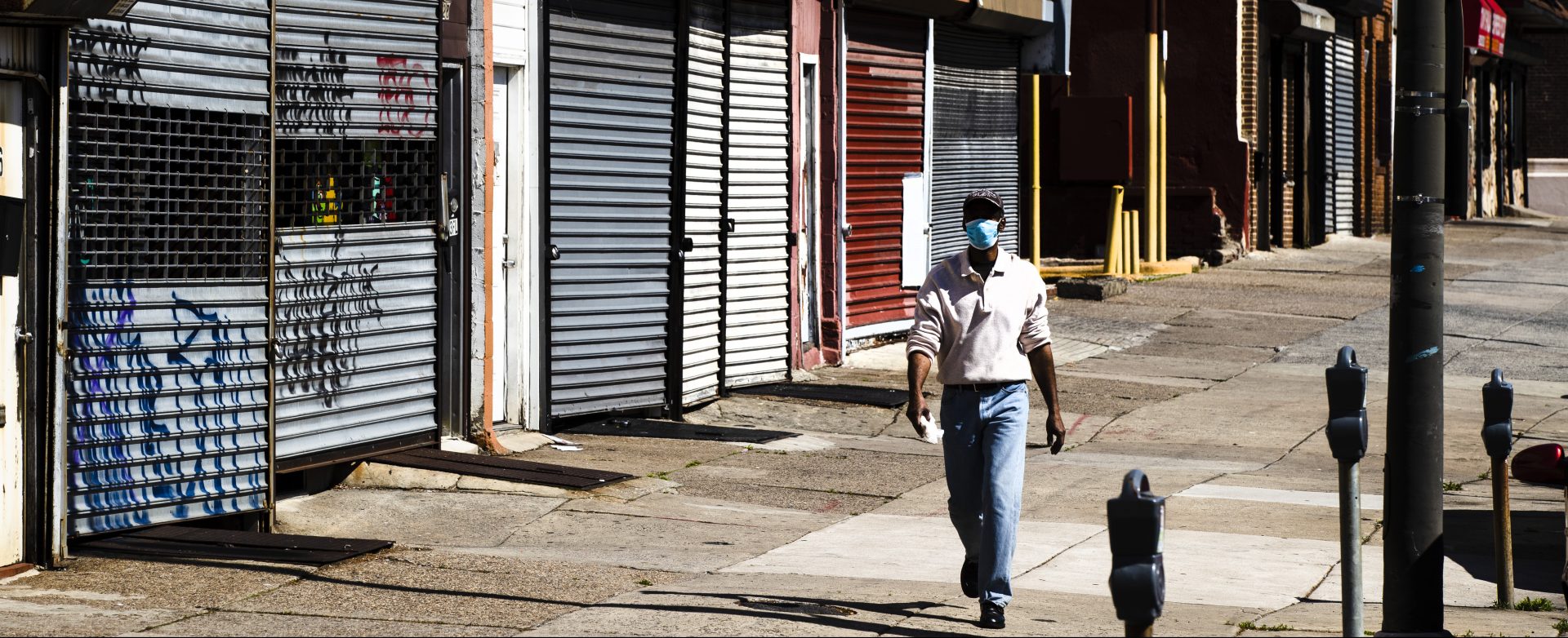 A person wearing a protective face mask as a precaution against the coronavirus walks past stuttered businesses in Philadelphia, Thursday, May 7, 2020.