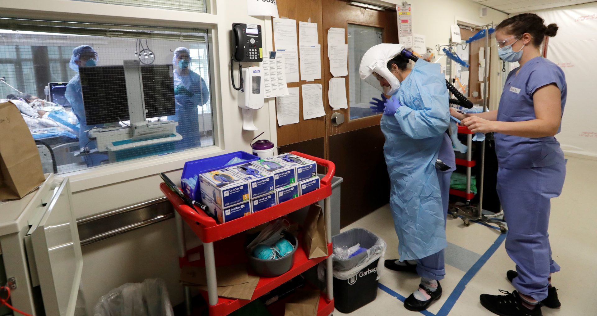 A medical worker is assisted into PPE while standing inside an area marked in blue tape, a "warm" area, before stepping into a patient's room in the COVID-19 Intensive Care Unit at Harborview Medical Center Friday, May 8, 2020, in Seattle.