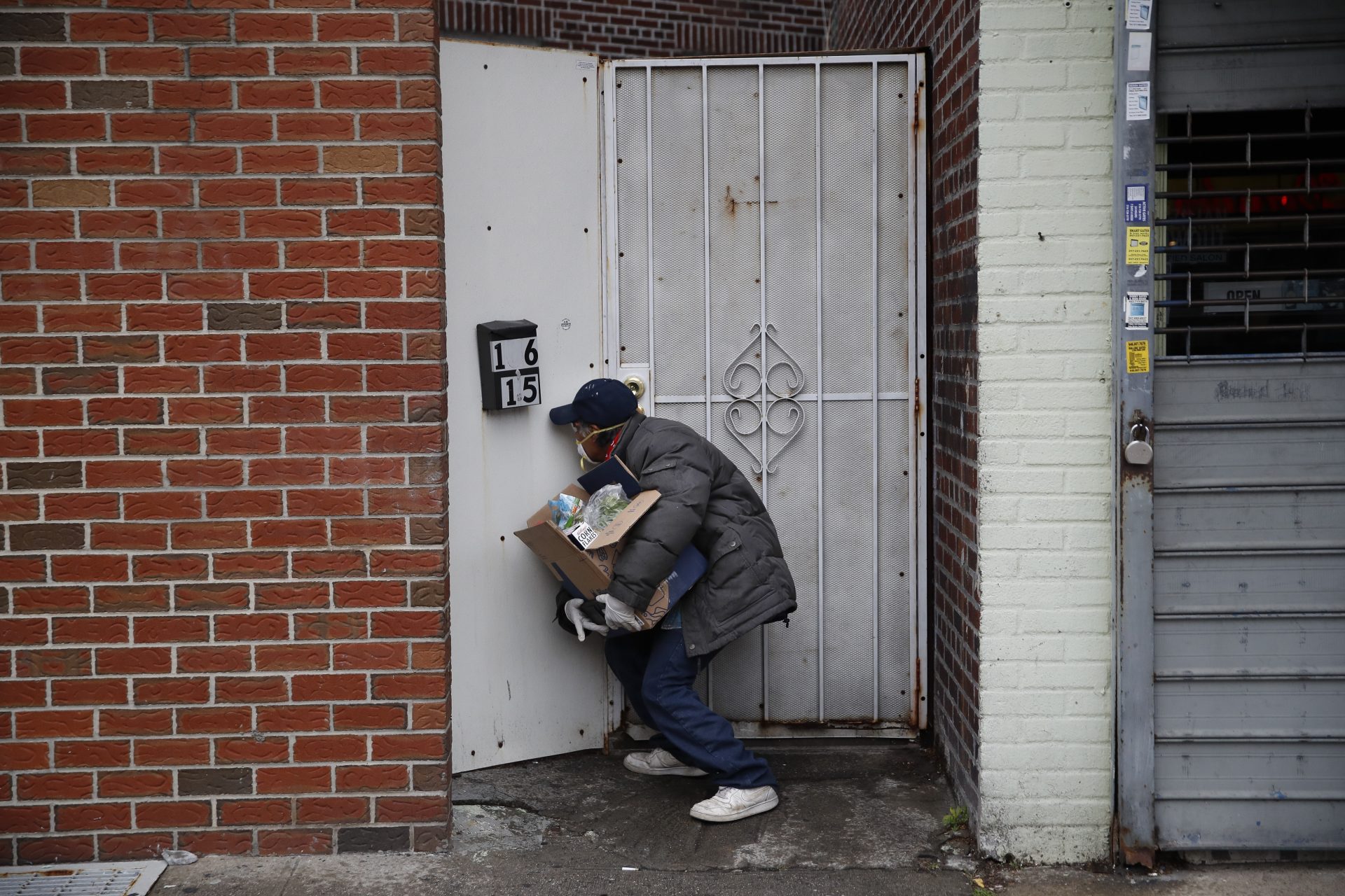 Francisco RamÃ­rez peers through a hole in a fence while looking for an address to deliver a box of groceries to a man in need Saturday, April 18, 2020, in the Queens borough of New York. Some are former construction workers or cleaning ladies who lost their jobs and can barely pay rent, but they go out each day to deliver donated diapers, formula or food to families in need. Through Spanish-speaking chats in Facebook or word of mouth, small groups of immigrants find out who needs the help and they deliver it traveling by car or by foot, exposing themselves to the coronavirus that has already hit hard working-class neighborhoods. (