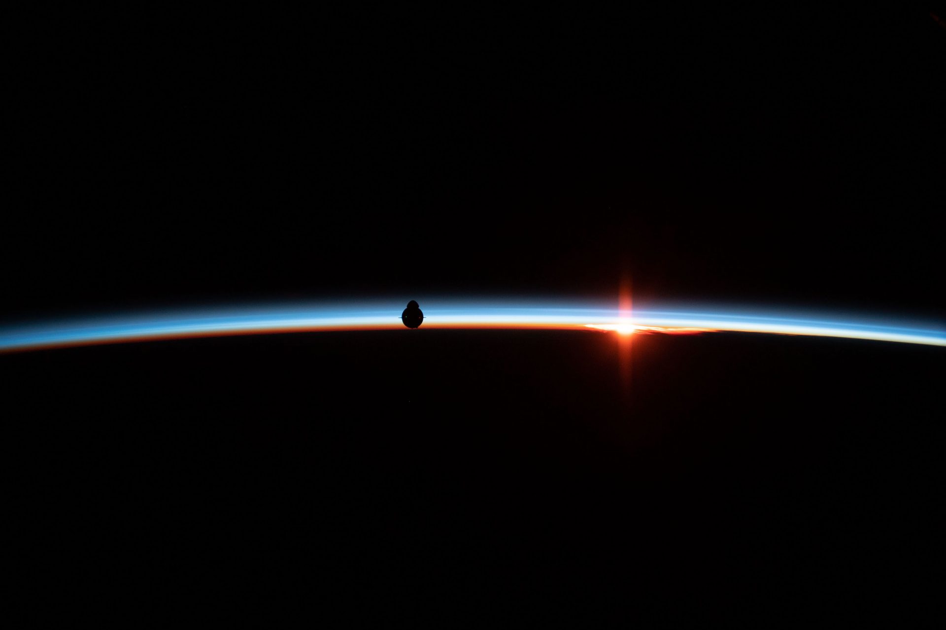 An uncrewed Dragon spacecraft is silhouetted against the Earth's horizon. The vehicle docked with the International Space Station and returned to Earth in 2019 as a dry run for the current mission.