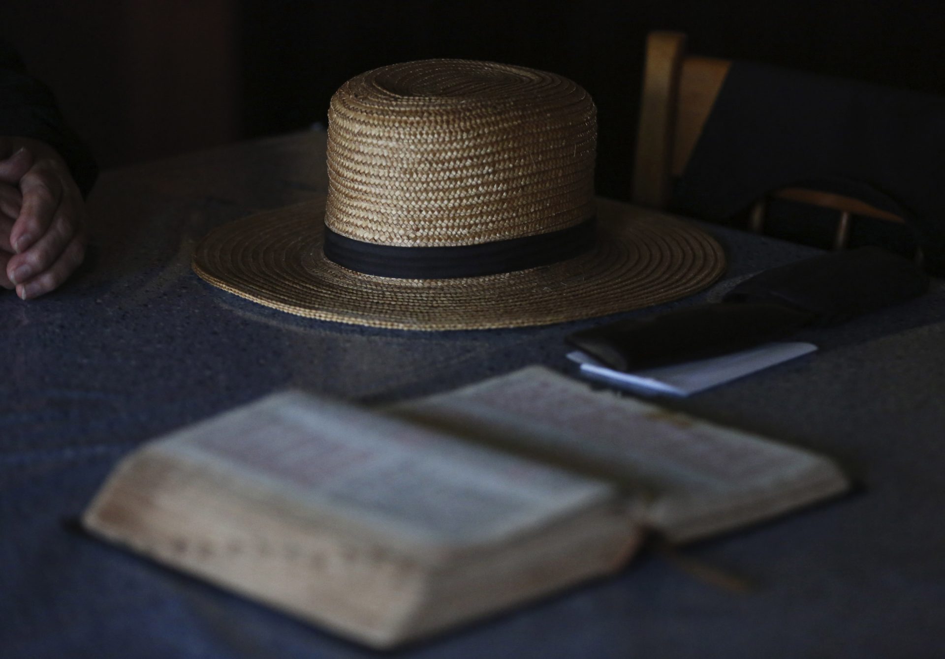 In this Saturday, May 16, 2020, photo, Bishop Marvin's straw hat sits on his living room table next to his Bible in German as he prepares for the Sunday service in Ephrata, Pa. The Old Order Stauffer Church, which shuns most modern technology including the internet, telephones and cars, has been isolated in the Mennonite Valley without church service as it followed the state's COVID-19 stay-at-home order. Gov. Tom Wolf's order exempted religious activity, but strongly discouraged gatherings. (