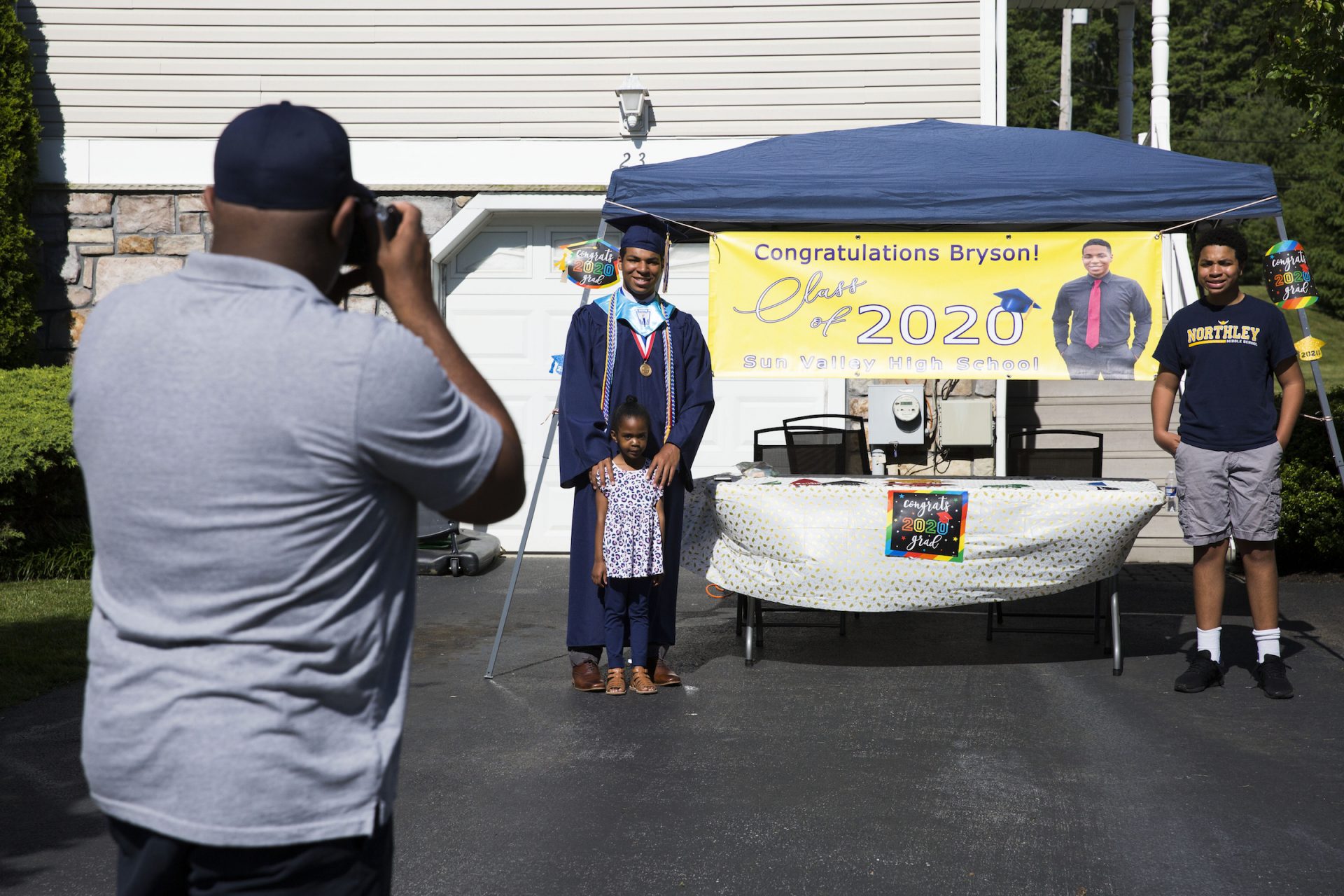 Greg Eldridge (left) takes a photo of his kids (from left) Bryson, Kennedy, and Blaise in the driveway of their home on June 9, 2020. Bryson Eldridge is graduating from Sun Valley High School this year and will be attending the University of Scranton in the fall. (Rachel Wisniewski for WHYY)