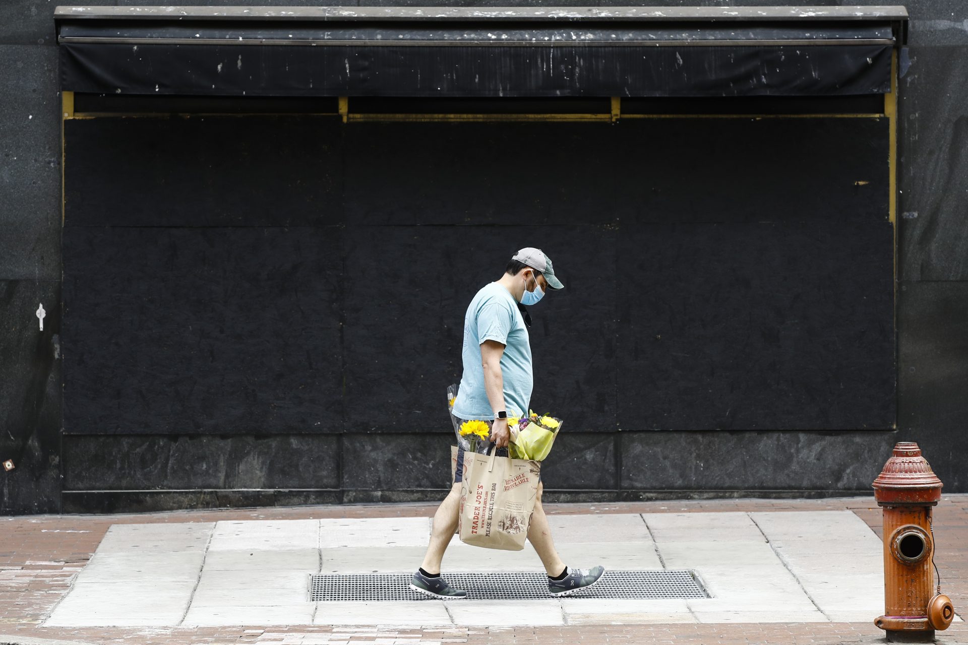 A person wearing a protective face mask as a precaution against the coronavirus walk past a boarded up business in Philadelphia, Thursday, May 21, 2020.