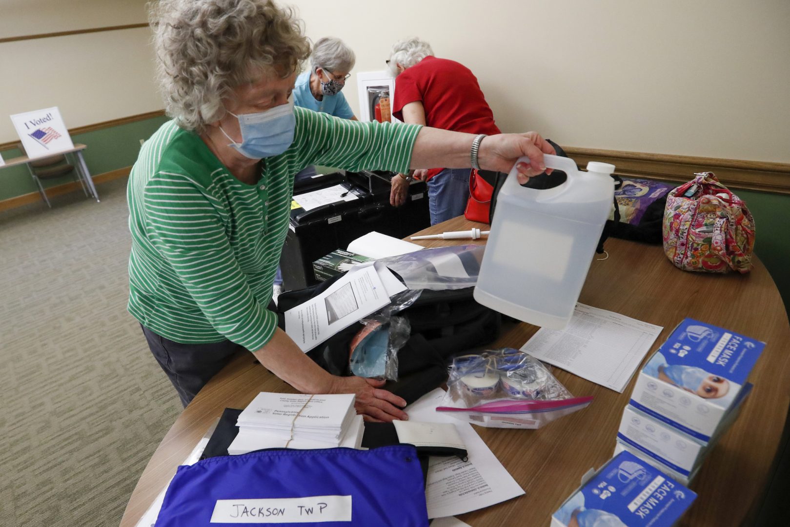Marty Goetz, left, unpacks a bottle of alcohol from the COVID-19 prep kit as they start to set up their polling place Monday, June 1, 2020, for the voting for Tuesday's Pennsylvania primary in Jackson Township near Zelienople, Pa. (AP Photo/Keith Srakocic)