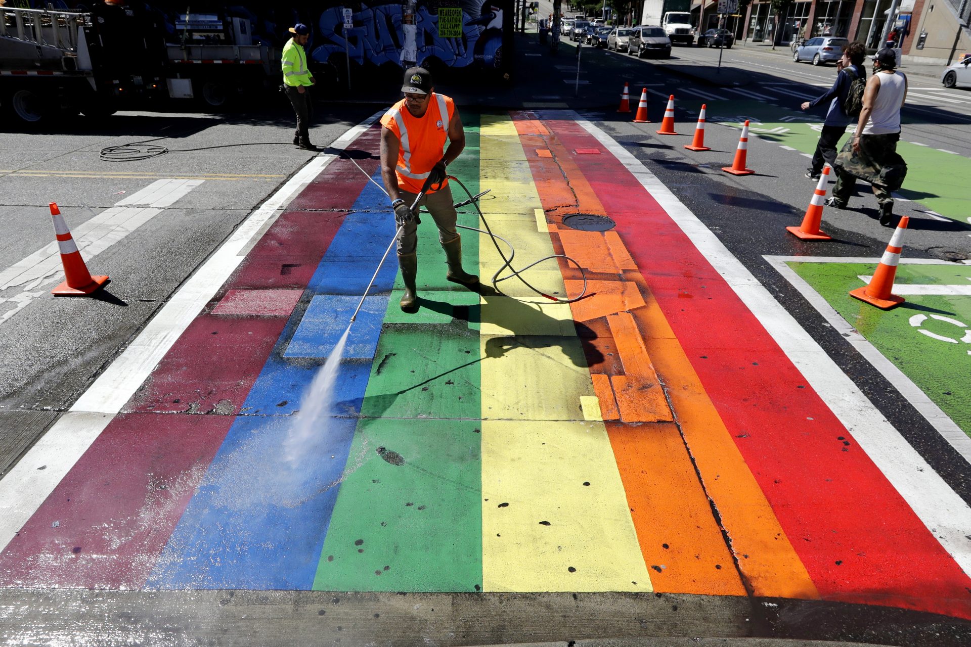 City worker Terrance Bryant pressure washes a rainbow-painted crosswalk in an annual clean-up ahead of Pride weekend Tuesday, June 23, 2020, in Seattle. The usual LGBTQ Pride weekend of events is being replaced with virtual events beginning Friday, June 26, with speakers, music and other online activities.