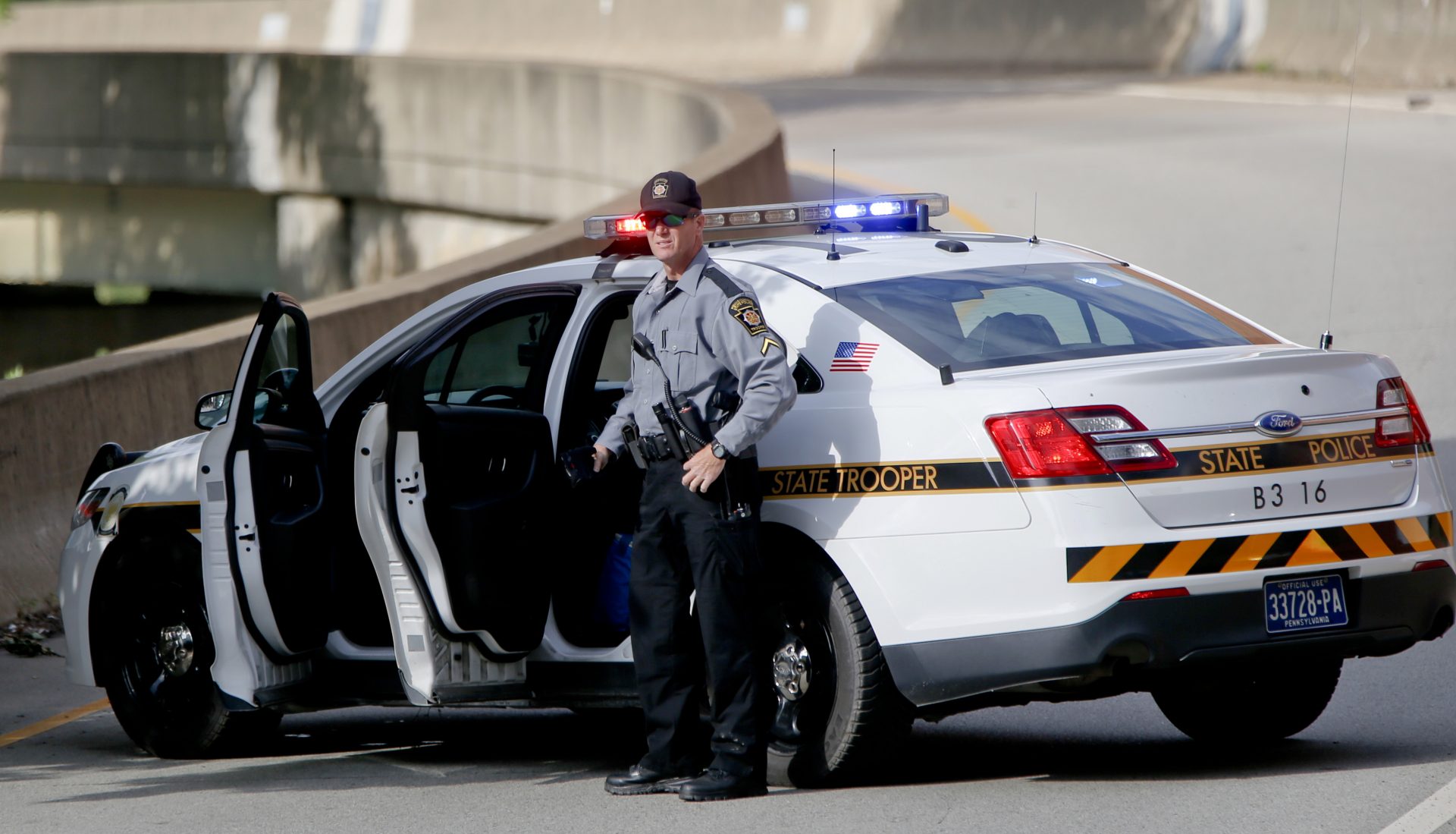 A Pennsylvania State Trooper stands beside his vehicle parked on the entrance ramp to Interstate 376 out of Pittsburgh as protesters block an intersection in downtown Pittsburgh, on Tuesday, June 26, 2018.