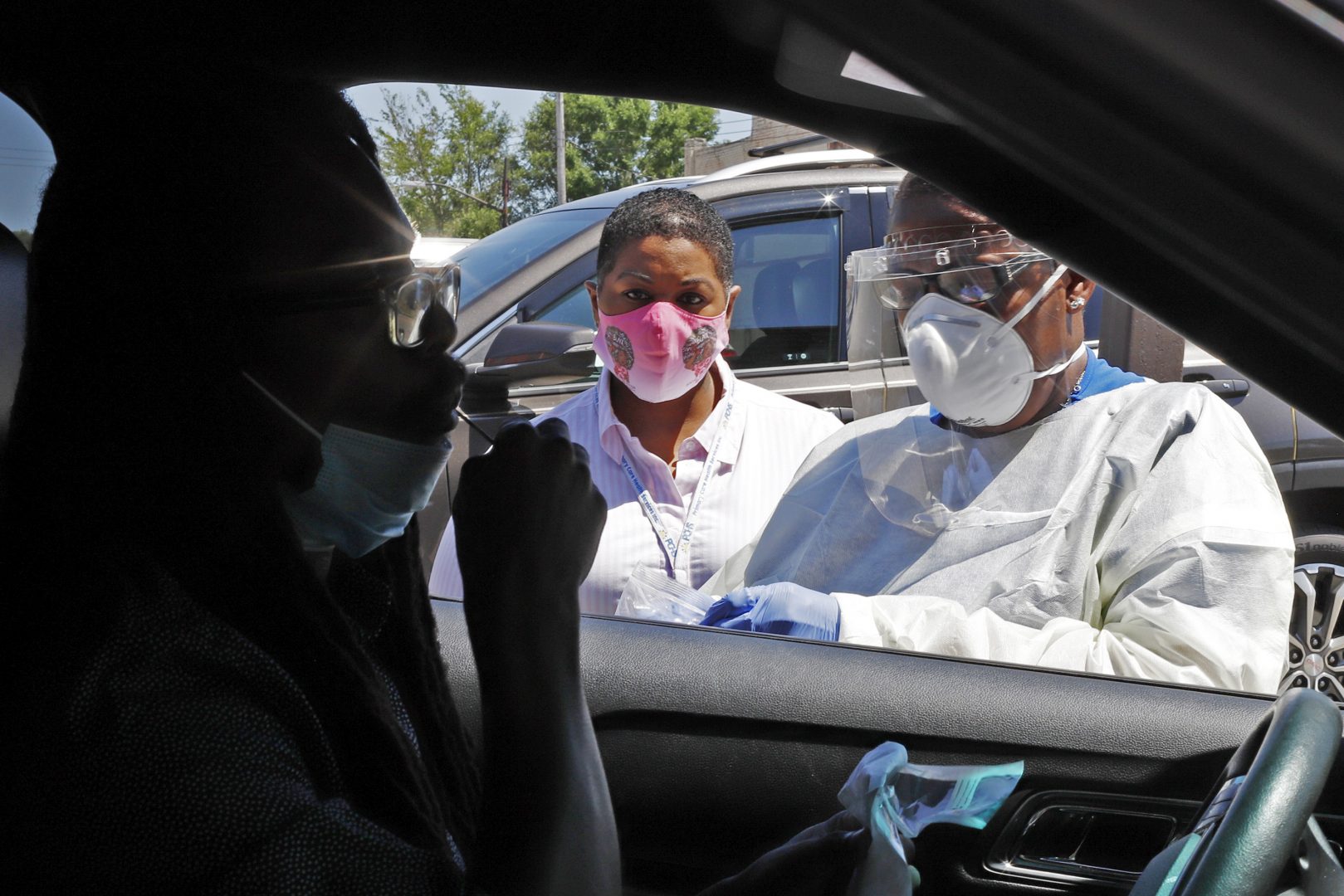 In this photo made on Monday, July 20, 2020, Kiva A. Fisher-Green, center, watches as nurse Ruth John, right, takes a sample from Walter Lewis for a COVID-19 test in the driveway of the Alma Illery Medical Center in the Homewood neighborhood of Pittsburgh.