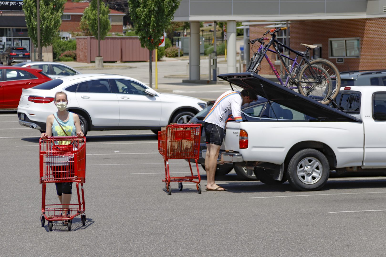 A woman and man wear COVID-19 protective masks as she pushes her shopping cart and a man loads his truck in a parking lot, Friday, July 3, 2020, in McCandless, Pa.