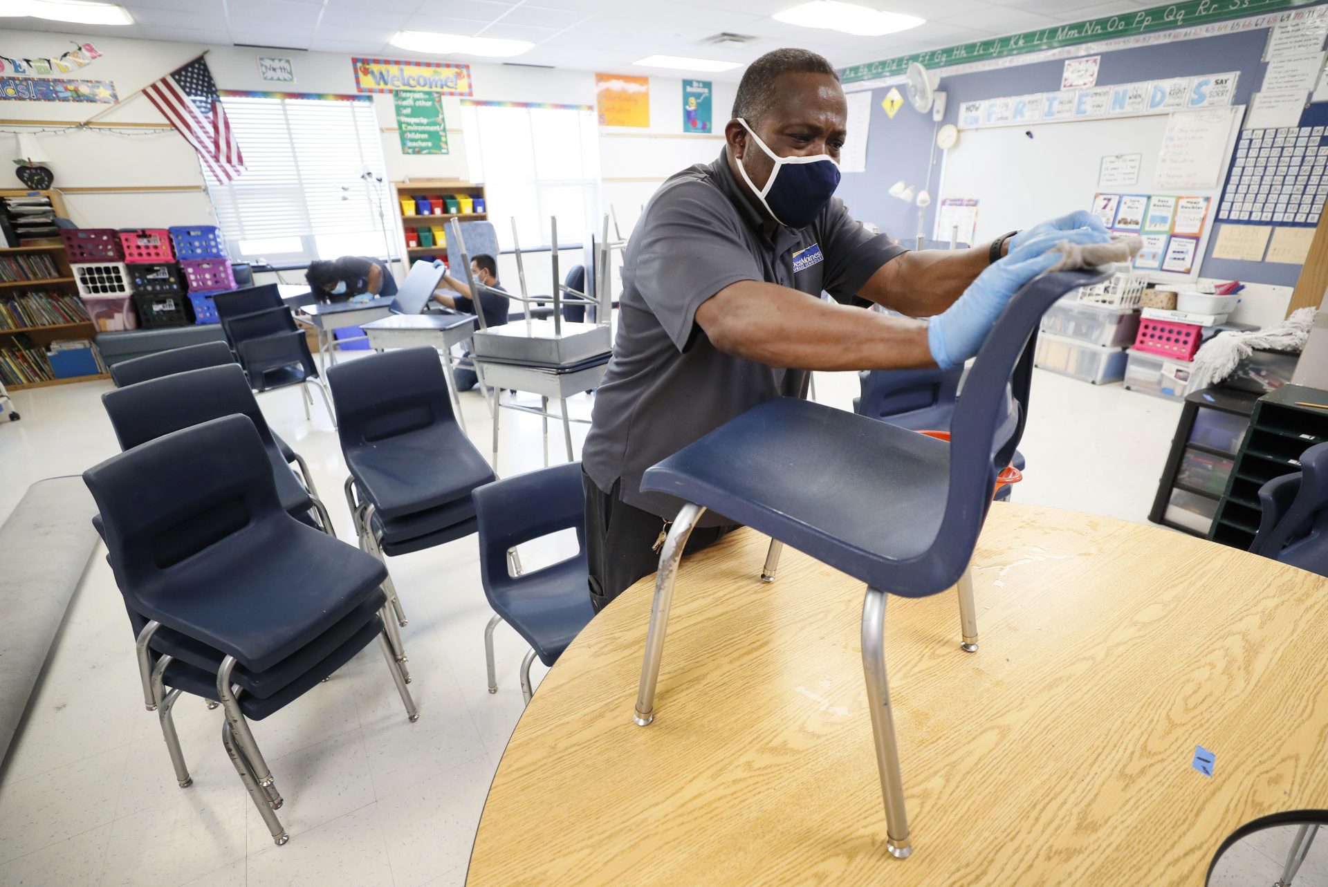 Des Moines Public Schools custodian Tracy Harris cleans chairs in a classroom at Brubaker Elementary School, Wednesday, July 8, 2020, in Des Moines, Iowa. Getting children back to school safely could mean keeping high-risk spots like bars and gyms closed. That's the latest thinking from some public health experts.