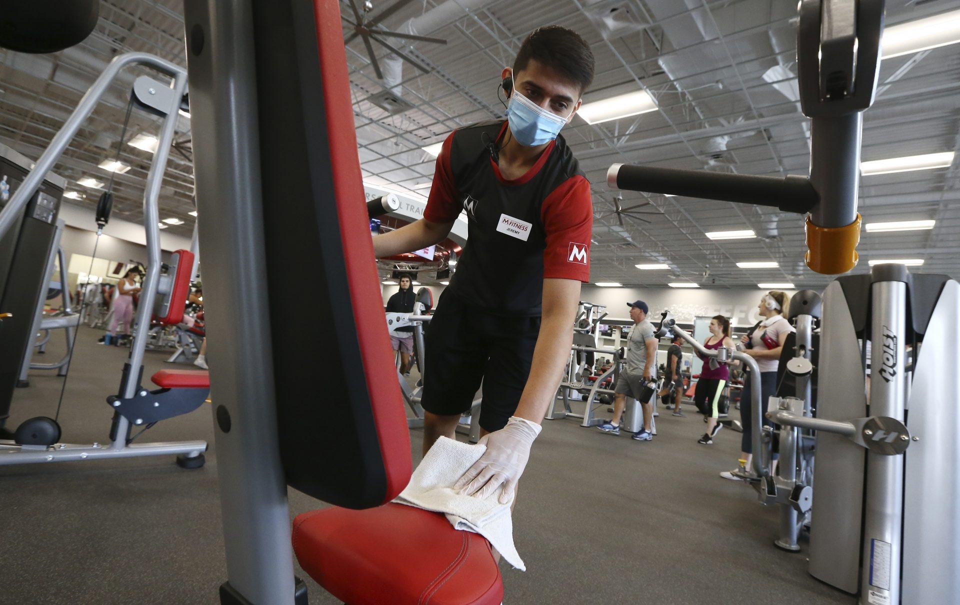 Jeremy Zepeda, a front desk associate at Mountainside Fitness, disinfects workout equipment as the facility remains open even as Arizona Gov. Doug Ducey has issued an executive order for all gyms to close due to the surge in coronavirus cases in Arizona Thursday, July 2, 2020, in Phoenix. For the third straight day, several health clubs in metro Phoenix were defying Ducey's 30-day shutdown order to close gyms, bars, water park and tubing businesses, raising questions about whether officials who have been criticized for responding indecisively to the pandemic will be effective in shutting down the clubs.