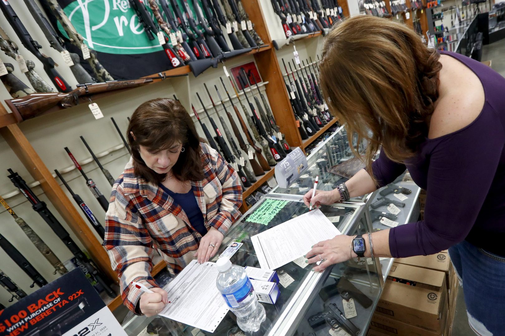 Andrea Schry, right, fills out the buyer part of legal forms to buy a handgun as shop worker Missy Morosky fills out the vendors parts after Dukes Sport Shop reopened, Wednesday, March 25, 2020, in New Castle, Pa.  