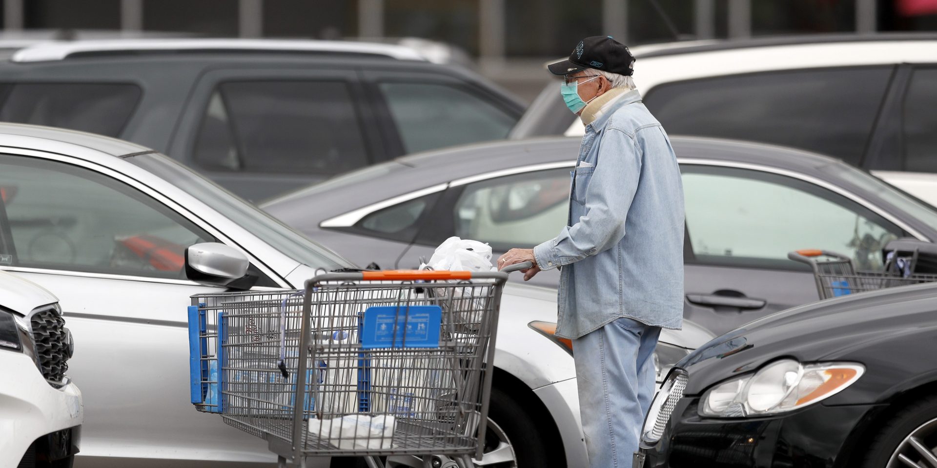 A man wears a face mask as he maneuvers his shopping cart between vehicles after shopping at a Walmart store, Tuesday, March 31, 2020, in Pearl, Miss. 