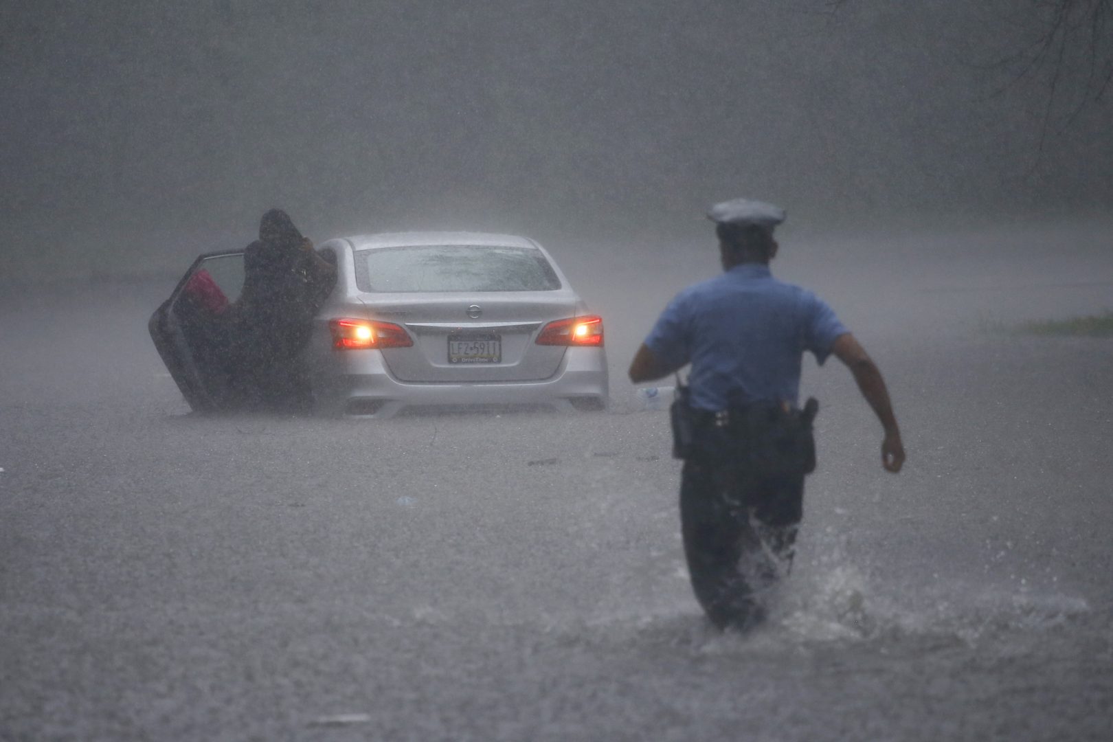 A Philadelphia police officer rushes to help a stranded motorist during Tropical Storm Isaias, Tuesday, Aug. 4, 2020, in Philadelphia. The storm spawned tornadoes and dumped rain during an inland march up the U.S. East Coast after making landfall as a hurricane along the North Carolina coast. 