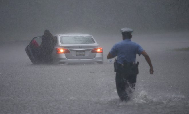 A Philadelphia police officer rushes to help a stranded motorist during Tropical Storm Isaias, Tuesday, Aug. 4, 2020, in Philadelphia. The storm spawned tornadoes and dumped rain during an inland march up the U.S. East Coast after making landfall as a hurricane along the North Carolina coast. 