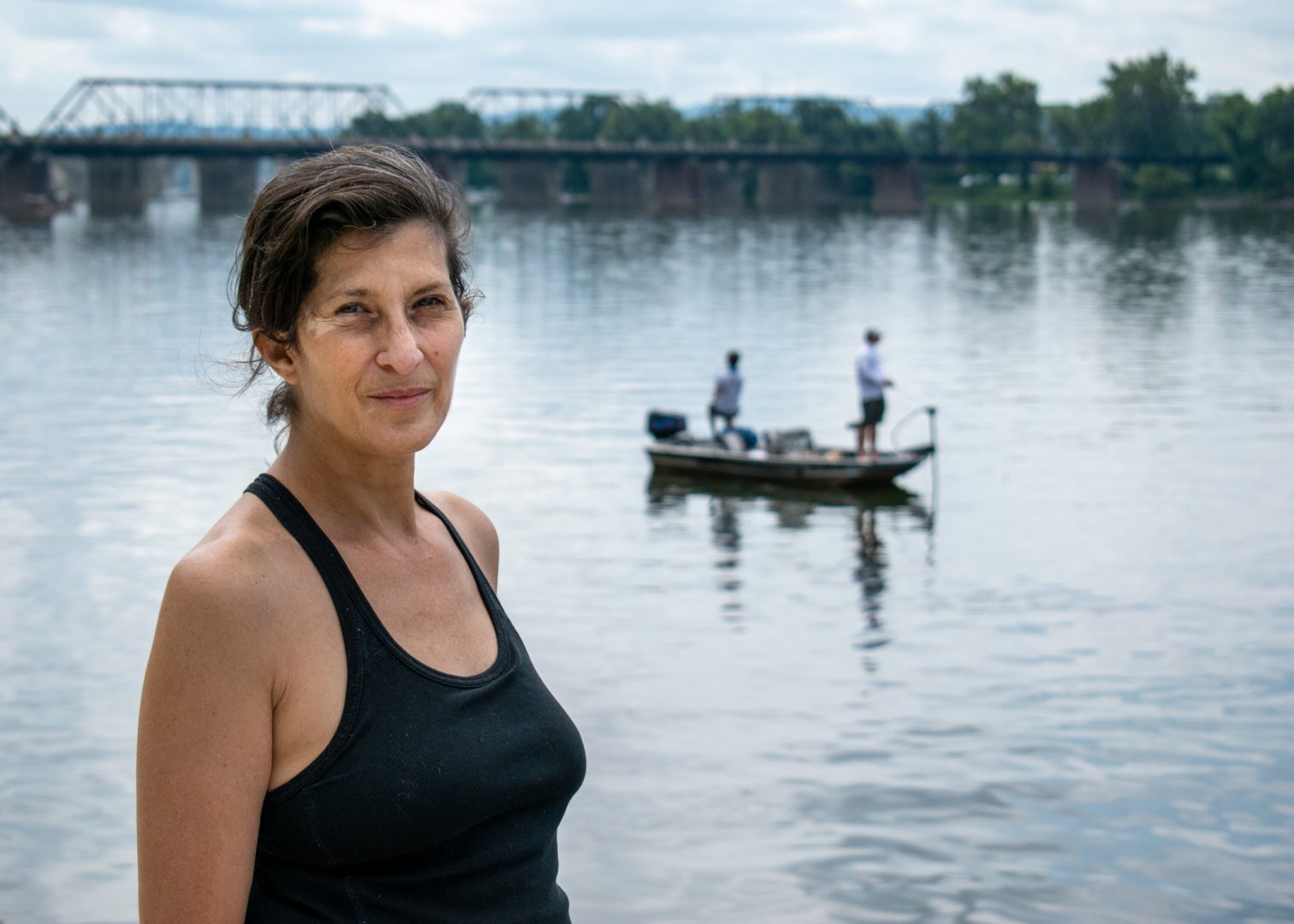 Ilyse Kazar stands along the Susquehanna river in Harrisburg next to a stormwater outflow while anglers fish nearby. Kazar, of Harrisburg, is one of the volunteers who collected water samples as part of the Lower Susquehanna Riverkeeper's annual water monitoring.