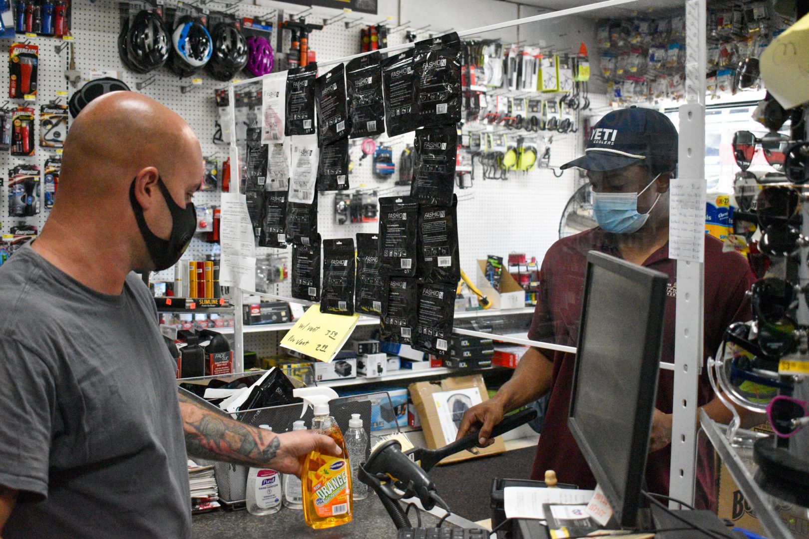 With a pane of clear plastic between them, Brandyn Hamilton, at right, buys some home cleaning products from David Arnold, at left, at Hornung's True Value Hardware in Harrisburg. 