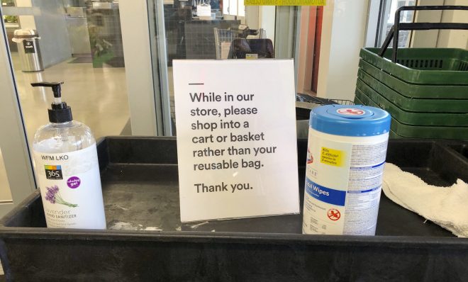 In this Sunday, March 29, 2020, photo, a sign posted at an entrance to a 365 Whole Foods store advises customers not to use their own bags while shopping in Lake Oswego, Ore. Just weeks earlier, cities and even states across the U.S. were busy banning straws, limiting takeout containers and mandating that shoppers bring reusable bags or pay a small fee. Grocery clerks became nervous that the virus could linger on reusable fabric bags, and their unions backed them up with demands to end plastic bag fees and suspend bag bans. The plastics industry seized the moment, lobbying to overturn existing bans on single-use plastics.  