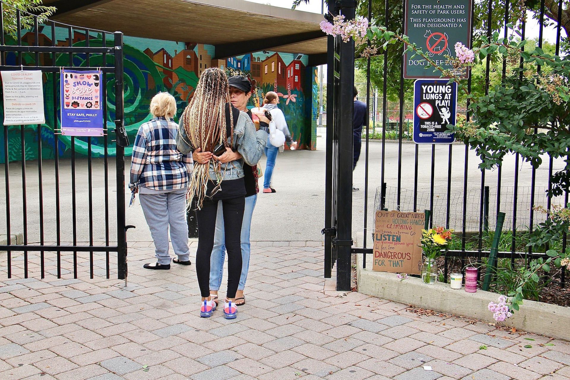 Neighbors embrace at the entrance to Roberto Clemente Playground, where two young men were killed and another three injured by gunfire that began on a basketball court.