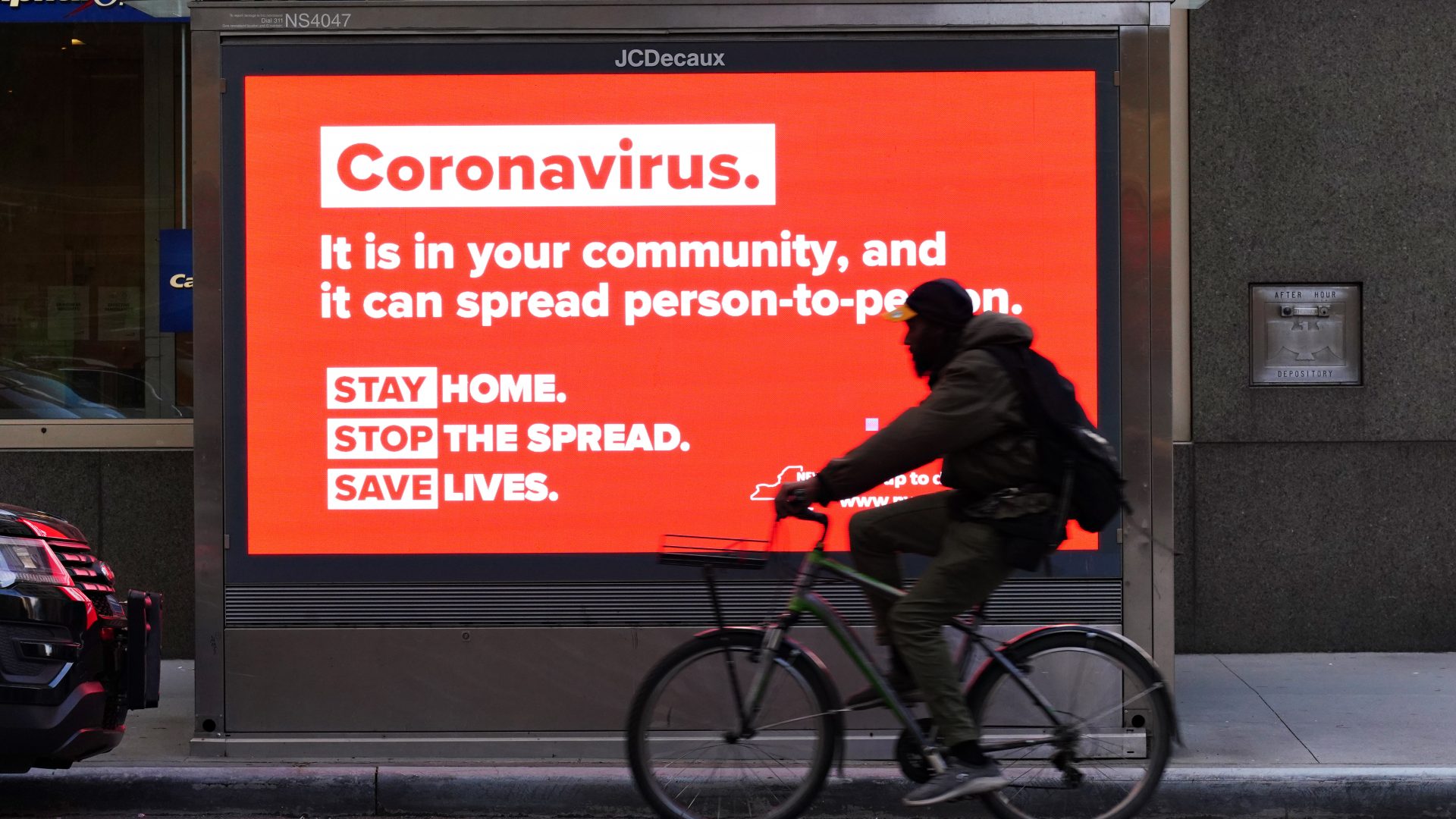 A person on a bike rides by a sign in New York City urging people to stay home in May. As the pandemic drags on, some workers are facing tough choices — balancing potential risks of unwittingly spreading the disease against the possibility of losing pay during a quarantine.