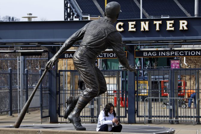 A woman sits on the base of a statue of Pittsburgh Pirates Hall of Fame outfielder Roberto Clemente outside the centerfield gate of PNC Park on the Northside of Pittsburgh, Wednesday, March 18, 2020.