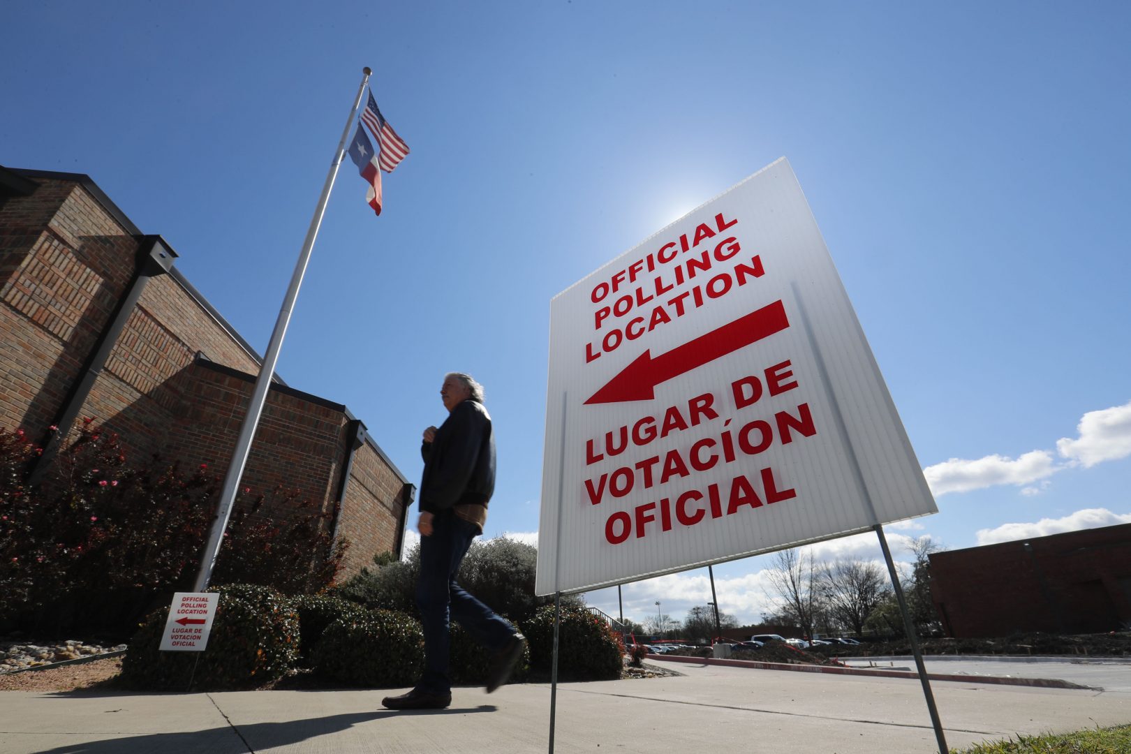 In this Feb. 26, 2020 file photo, using both the English and Spanish language, a sign points potential voters to an official polling location during early voting in Dallas.  Getting enough people to staff polling places amid the coronavirus pandemic is a challenge in many states. The virus’ disproportionate impact on Latinos has made the task of recruiting Spanish-speakers even more difficult. 
