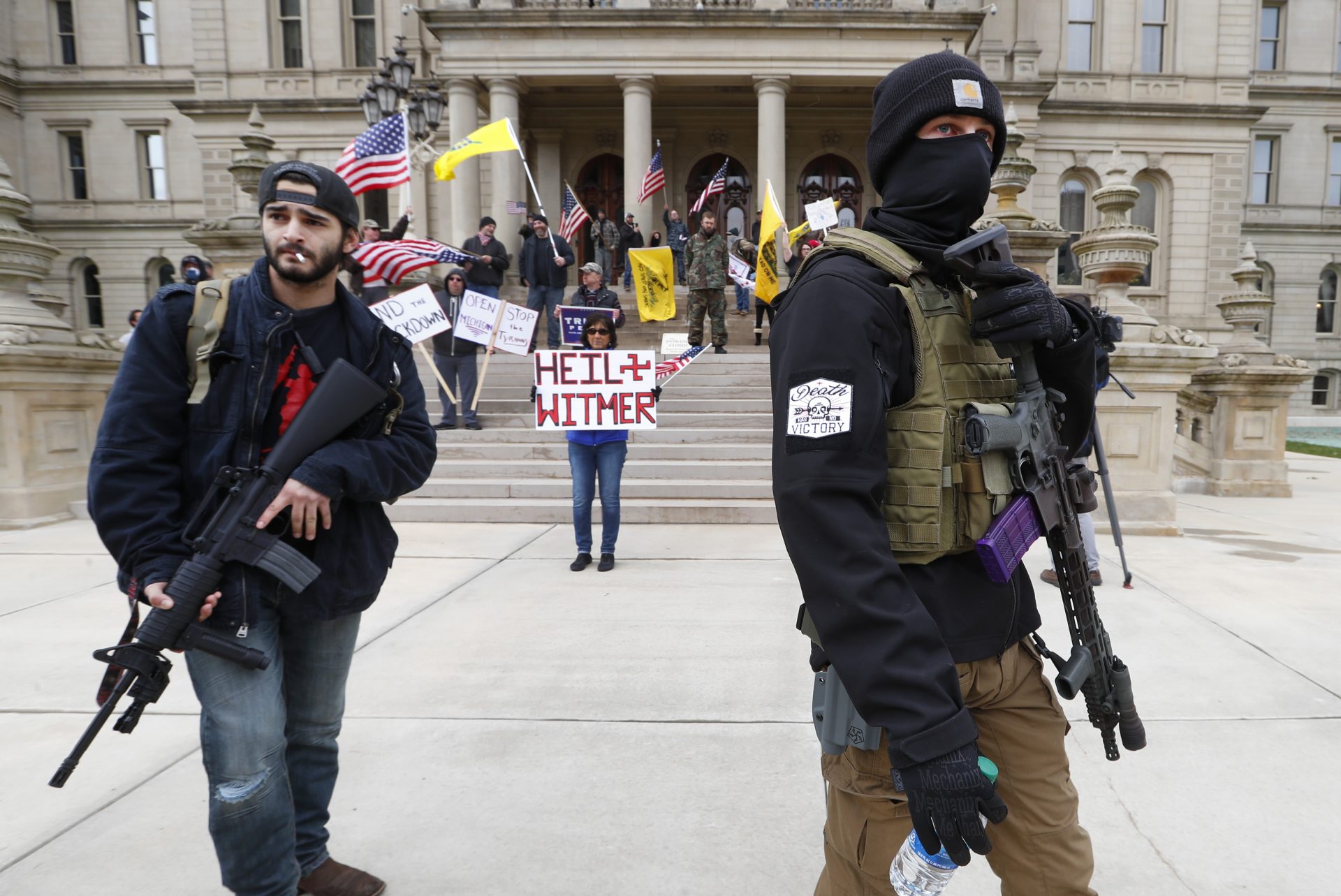 In this April 15, 2020 file photo, protesters carry rifles near the steps of the Michigan State Capitol building in Lansing, Mich. A plot to kidnap Michigan’s governor has put a focus on the security of governors who have faced protests and threats over their handling of the coronavirus pandemic. The threats have come from people who oppose business closures and restrictions on social gatherings.