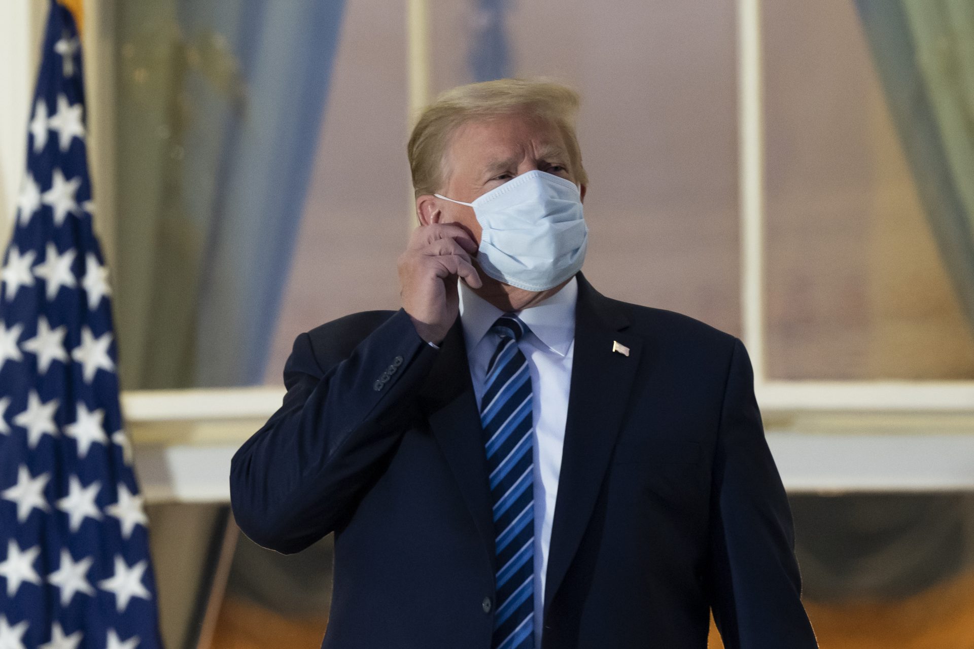 President Donald Trump removes his mask as he stands on the Blue Room Balcony upon returning to the White House Monday, Oct. 5, 2020, in Washington, after leaving Walter Reed National Military Medical Center, in Bethesda, Md. Trump announced he tested positive for COVID-19 on Oct. 2.