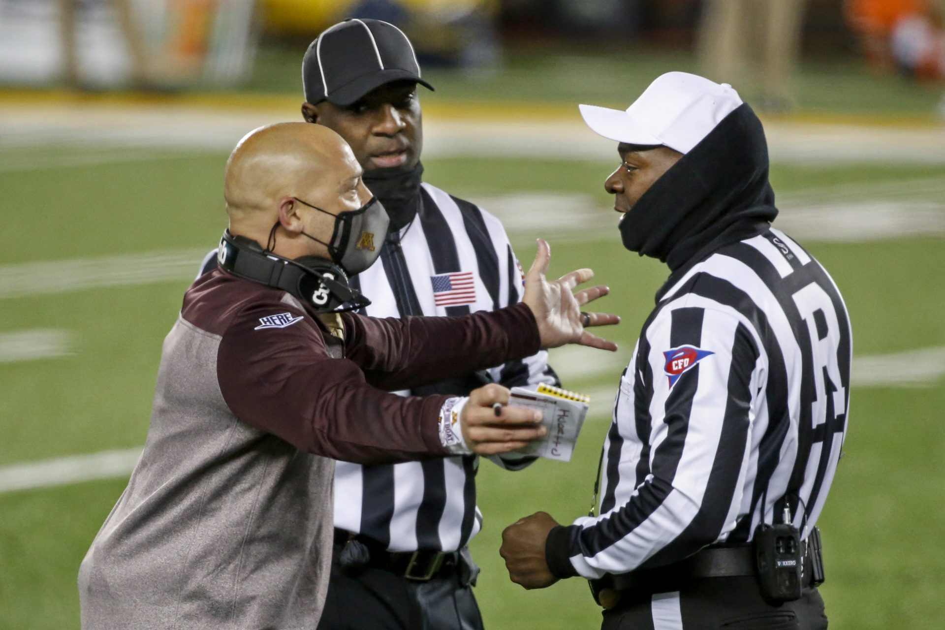 Minnesota head coach P.J. Fleck has a discussion with referee Larry Smith and headline judge William McKoy during a break in action at an NCAA college football game with Michigan Saturday, Oct. 24, 2020, in Minneapolis.