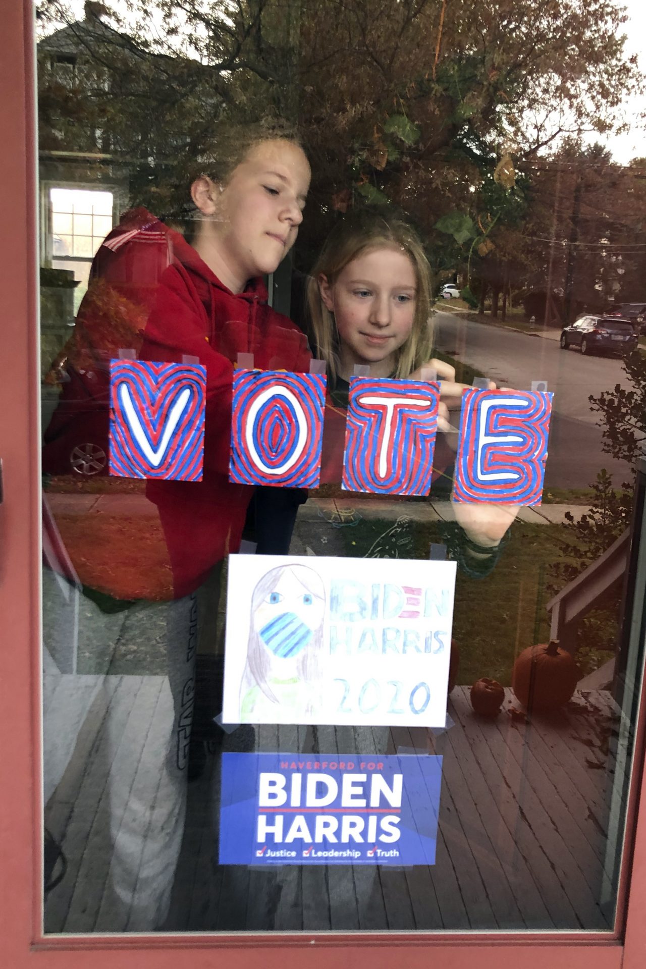 Sisters Maya and Julia Schmitt tape homemade signs on their home's front storm door on Election Day Tuesday Nov. 3, 2020, in the Philadelphia suburb of Havertown, Pa.
