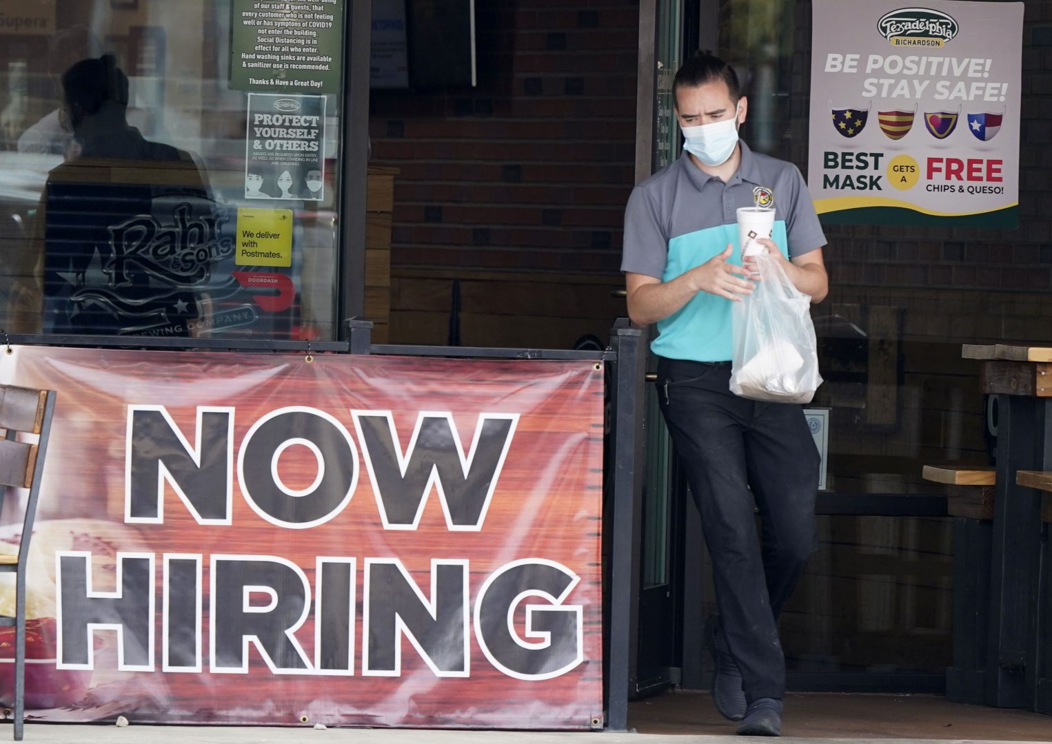 A customer wears a face mask as they carry their order past a now hiring sign at an eatery in Richardson, Texas.  On Thursday, Nov. 5, the number of Americans seeking unemployment benefits fell slightly last week to 751,000, a still-historically high level that shows that many employers keep cutting jobs in the face of the accelerating pandemic. 
