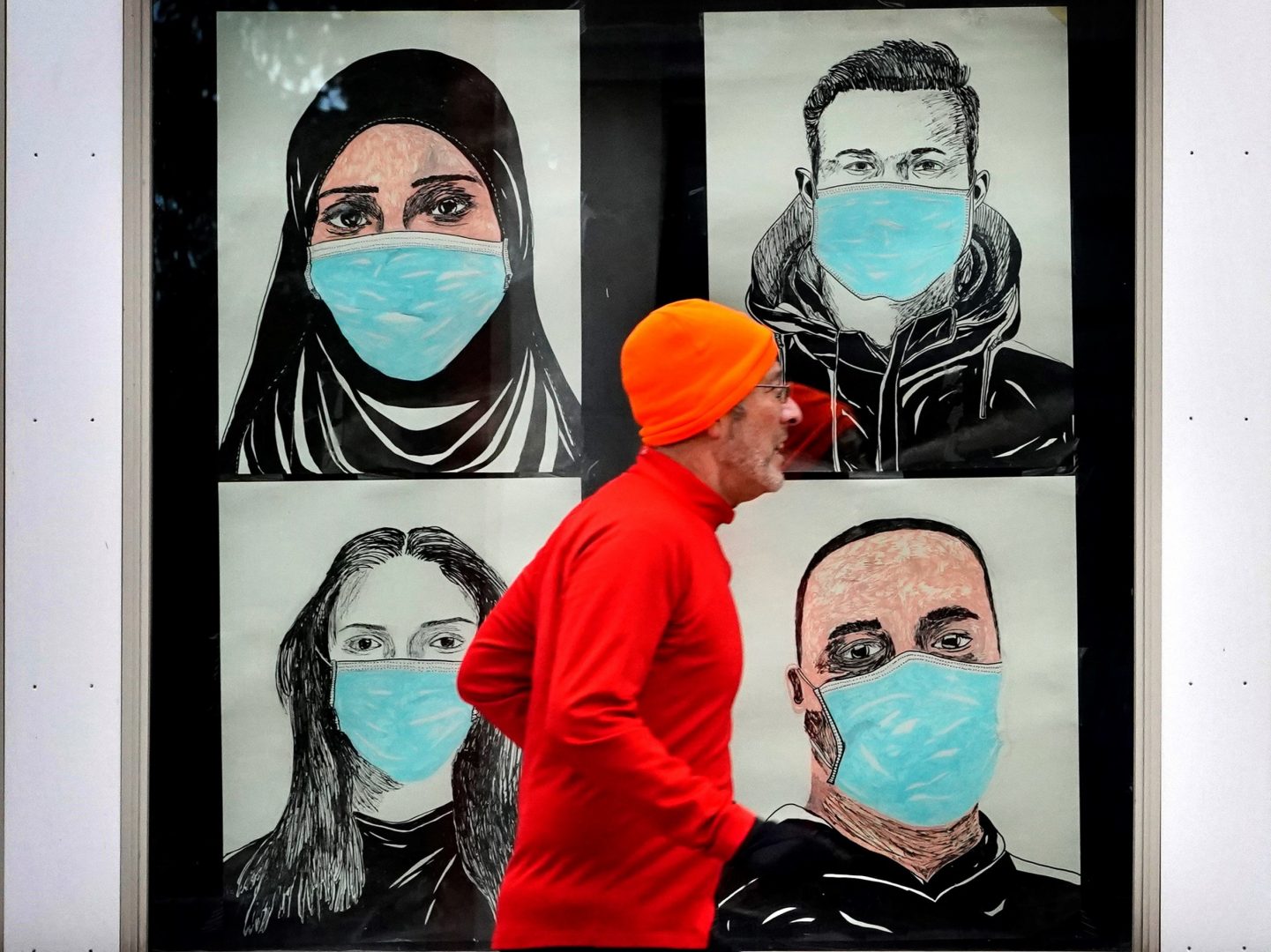 A runner passes by a window displaying portraits of people wearing face coverings to help prevent the spread of the coronavirus, Monday, Nov. 16, 2020, in Lewiston, Maine.