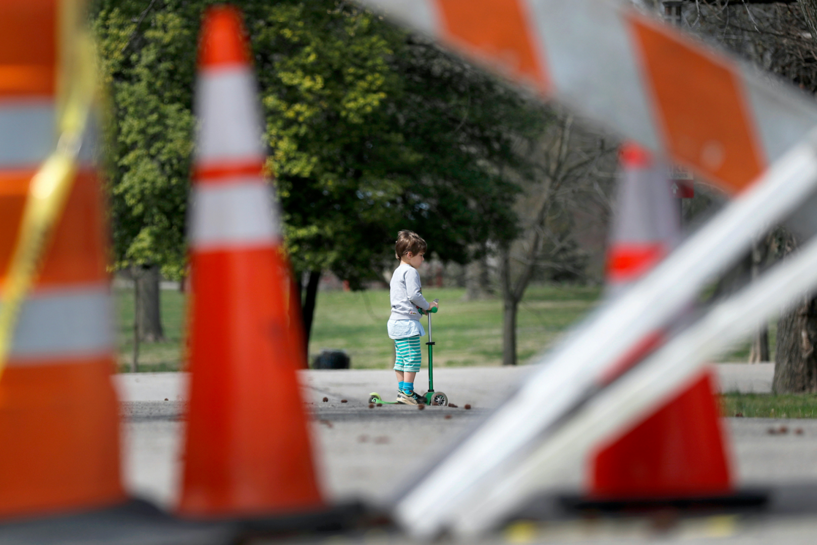 In this March 31, 2020 file photo, a child rides a scooter past barricades at an entrance to Tower Grove Park in St. Louis. 