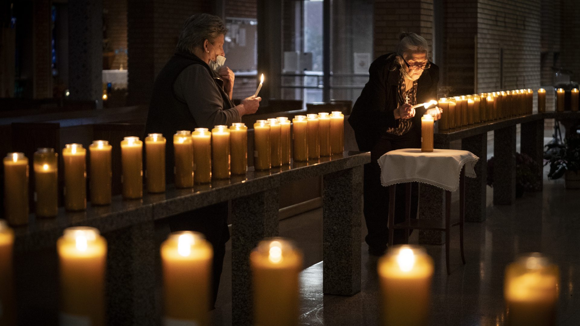 MINNEAPOLIS, MN,- NOVEMBER 2 - Left to right, Jodi Sandlin lit some of the more than 100 candles for loved ones of parish members who have died as Cece Ryan lit a candle in remembrance of those who died of Covid-19 during an All Souls Day service at St Bridget Catholic Church in Minneapolis, Minn., on Monday, November 2, 2020. These candles were for people who have died over the years.