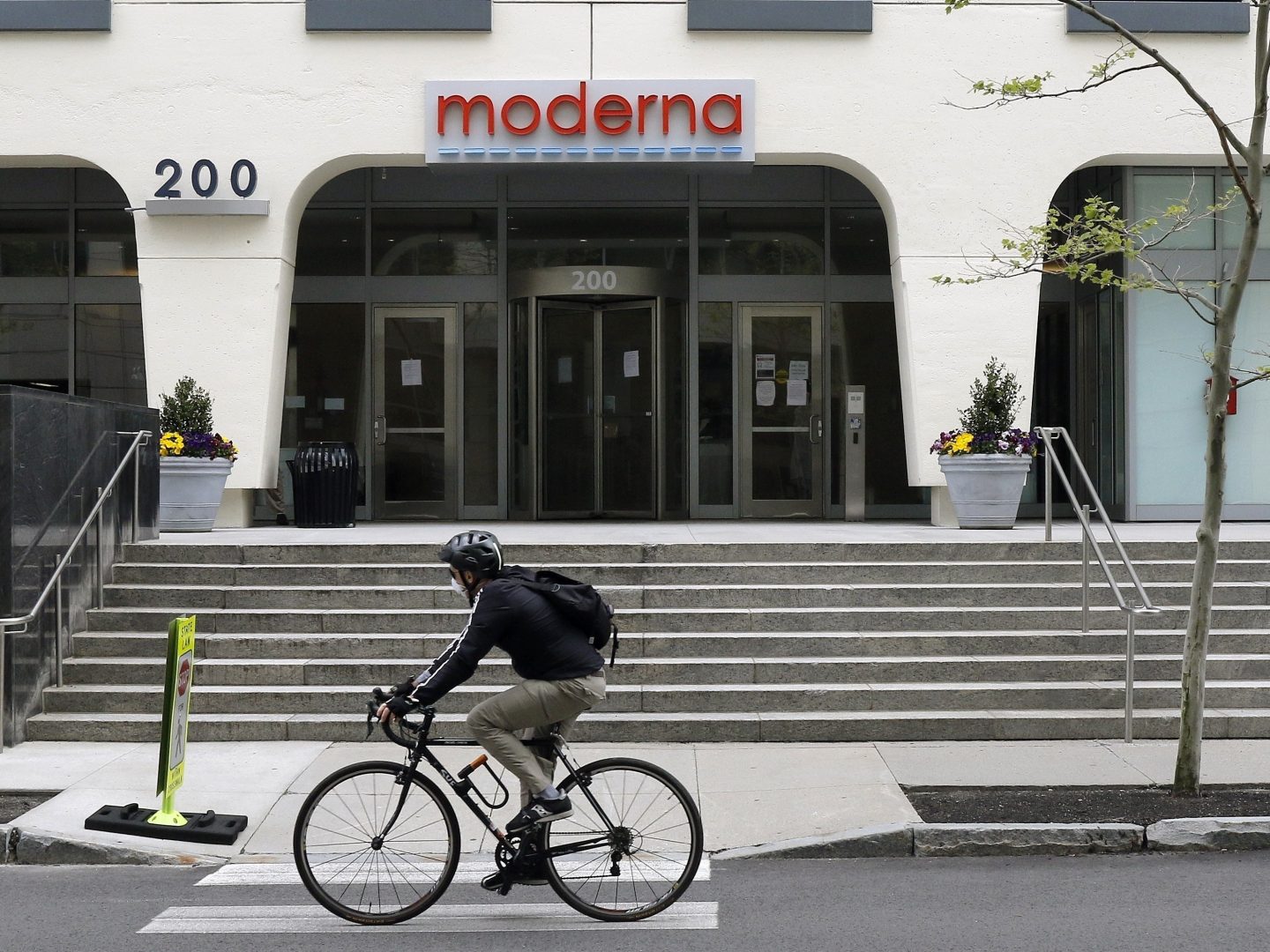 FILE PHOTO: In this May 18, 2020, file photo, a bicyclist pedals past an entrance to a Moderna, Inc., building in Cambridge, Mass.