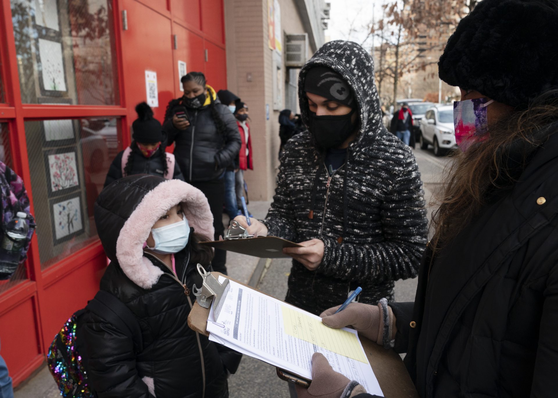 A parent, center, completes a form granting permission for random COVID-19 testing for students as he arrives with his daughter, left, at P.S. 134 Henrietta Szold Elementary School, Monday, Dec. 7, 2020, in New York.