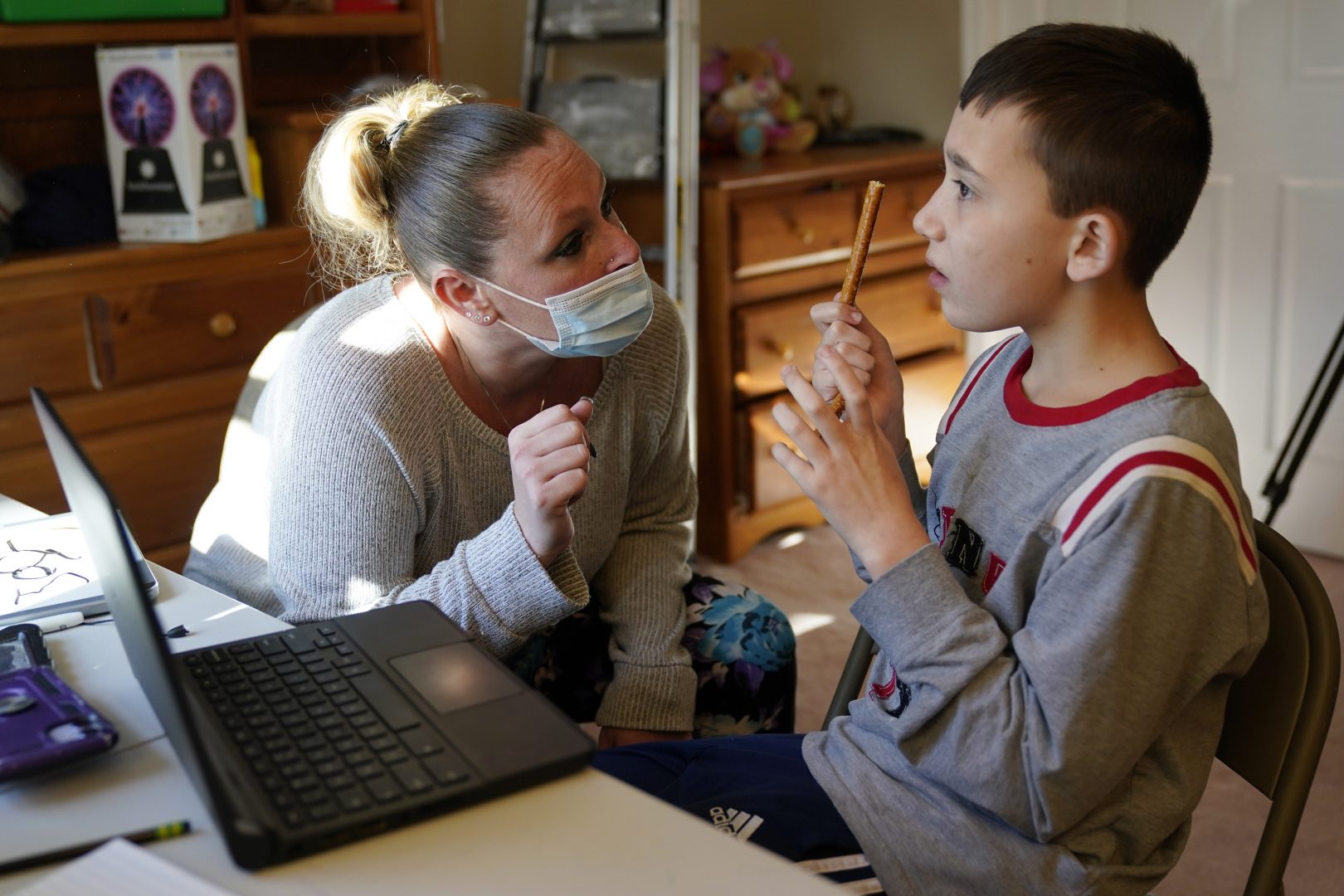 In this Associcated Press photo, paraprofessional Jessica Wein helps Josh Nazzaro, who lives with autism, with his classwork while attending class virtually from his home in Wharton, N.J., Wednesday, Nov. 18, 2020.  In Pa., a change  a state policy change is barring some children with autism from being covered by Medical Assistance for a type of one-on-one therapy.