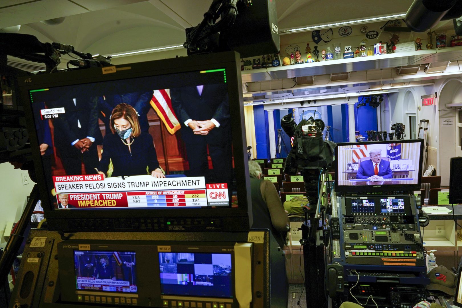 President Donald Trump is seen speaking on a television monitor in an empty press briefing room at the White House in Washington, from a video statement released by President Donald Trump on Twitter as it is broadcast by FOX News, after the U.S. House impeached him, Wednesday, Jan. 13, 2021. At left is a replay of House Speaker Nancy Pelosi signing the article of impeachment, as broadcast by CNN. 