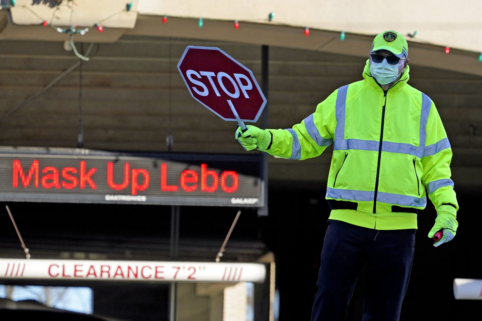 A school crossing guard works, Wednesday, Nov. 18, 2020, in Mount Lebanon, Pa., in front of a sign reminding people to wear a mask.